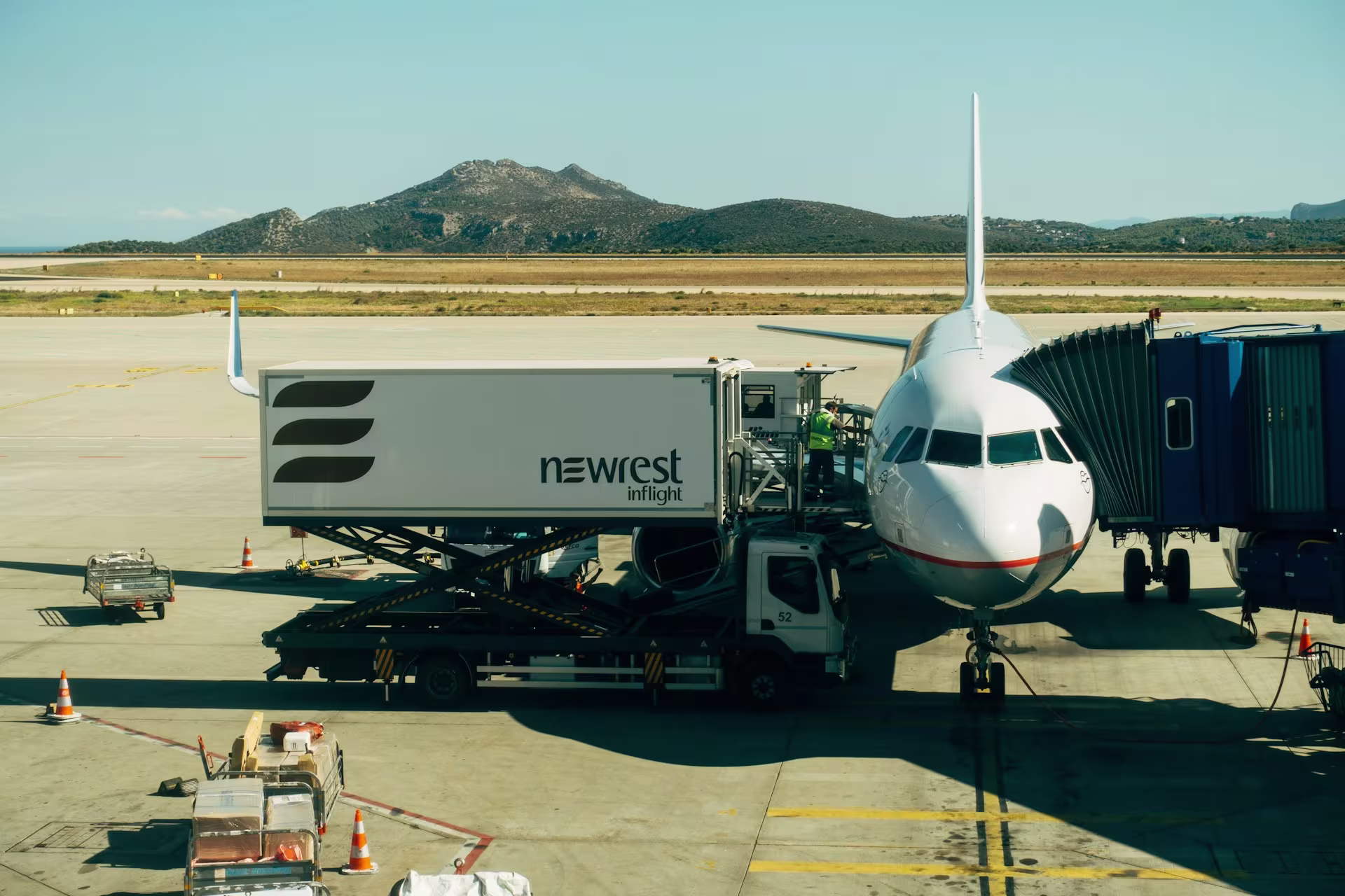 An airplane parked at an airport gate with a catering truck attached to load inflight meals