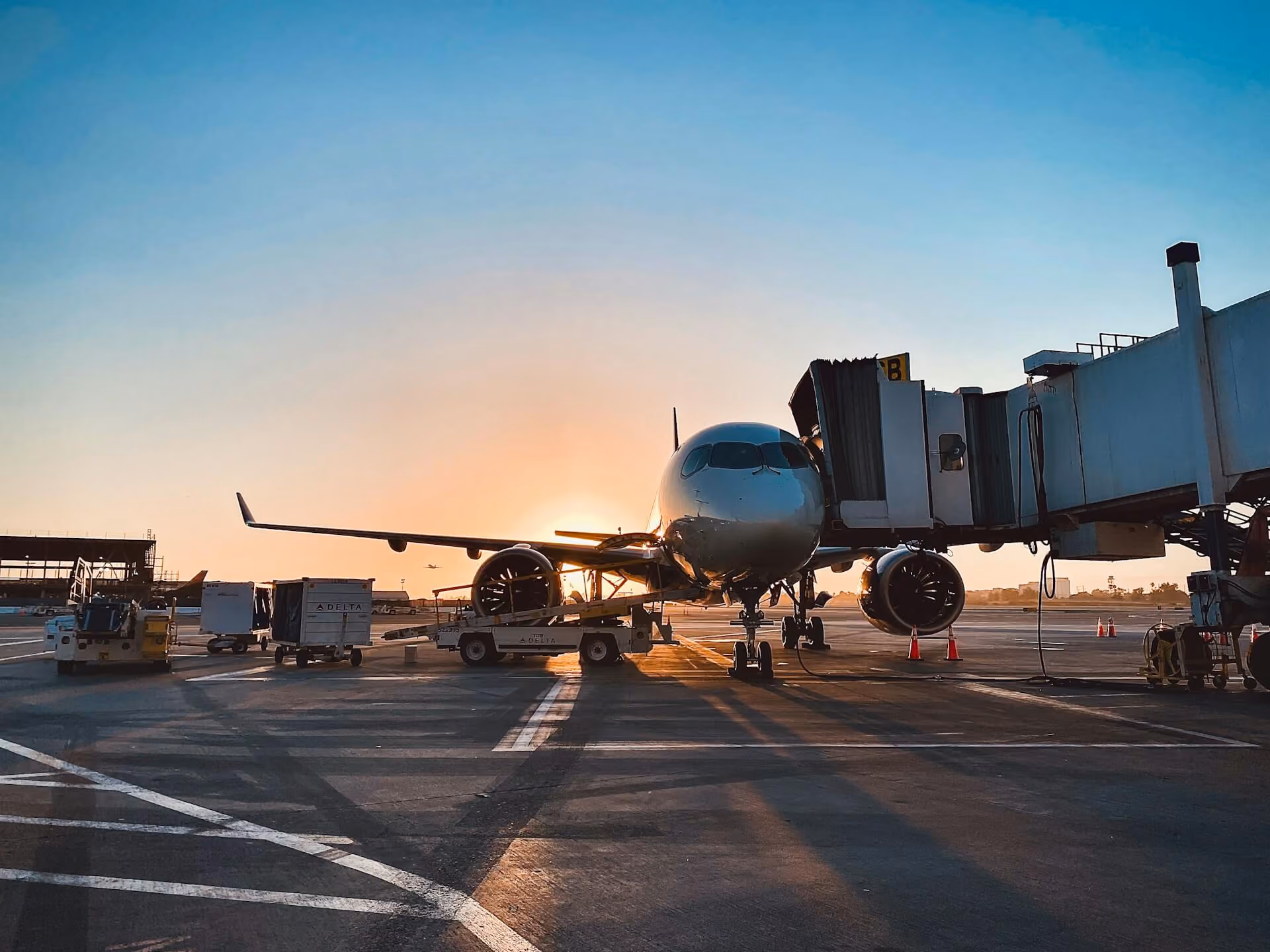 A commercial airplane parked at an airport terminal gate attached to a jet bridge during sunset