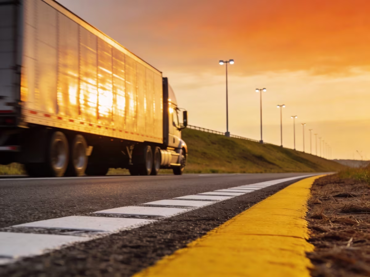 Side view of a semi-truck driving along an open highway during a vibrant golden sunset