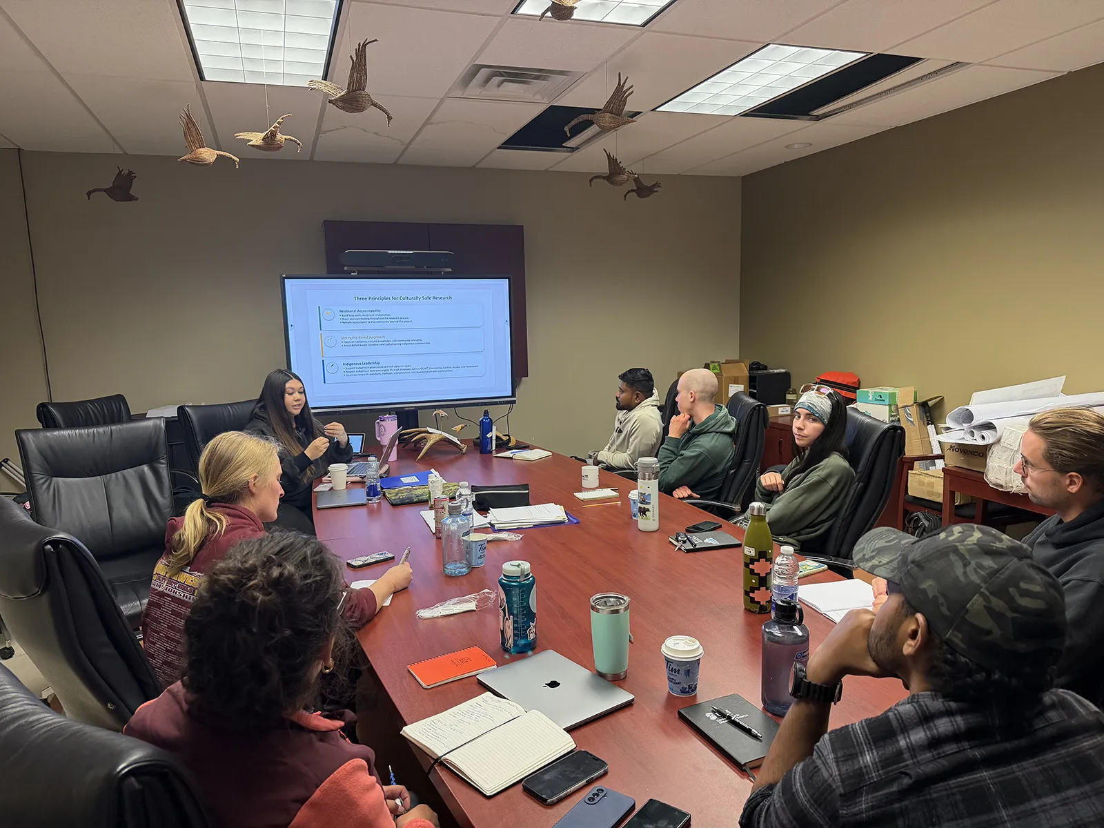 Group of people seated around a conference table watching a presentation on cultural safety research.
