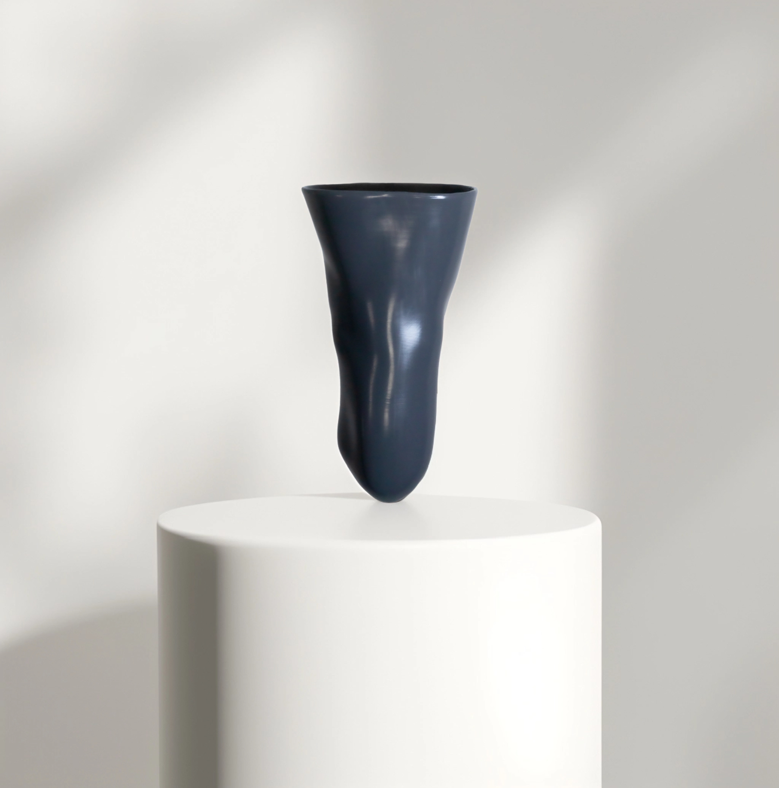 Dark gray silicone liner with a smooth surface positioned above a white pedestal against a neutral background.