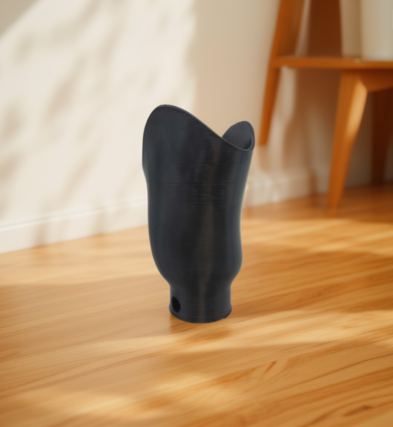 Black below-knee prosthetic socket standing upright on a wooden floor indoors.