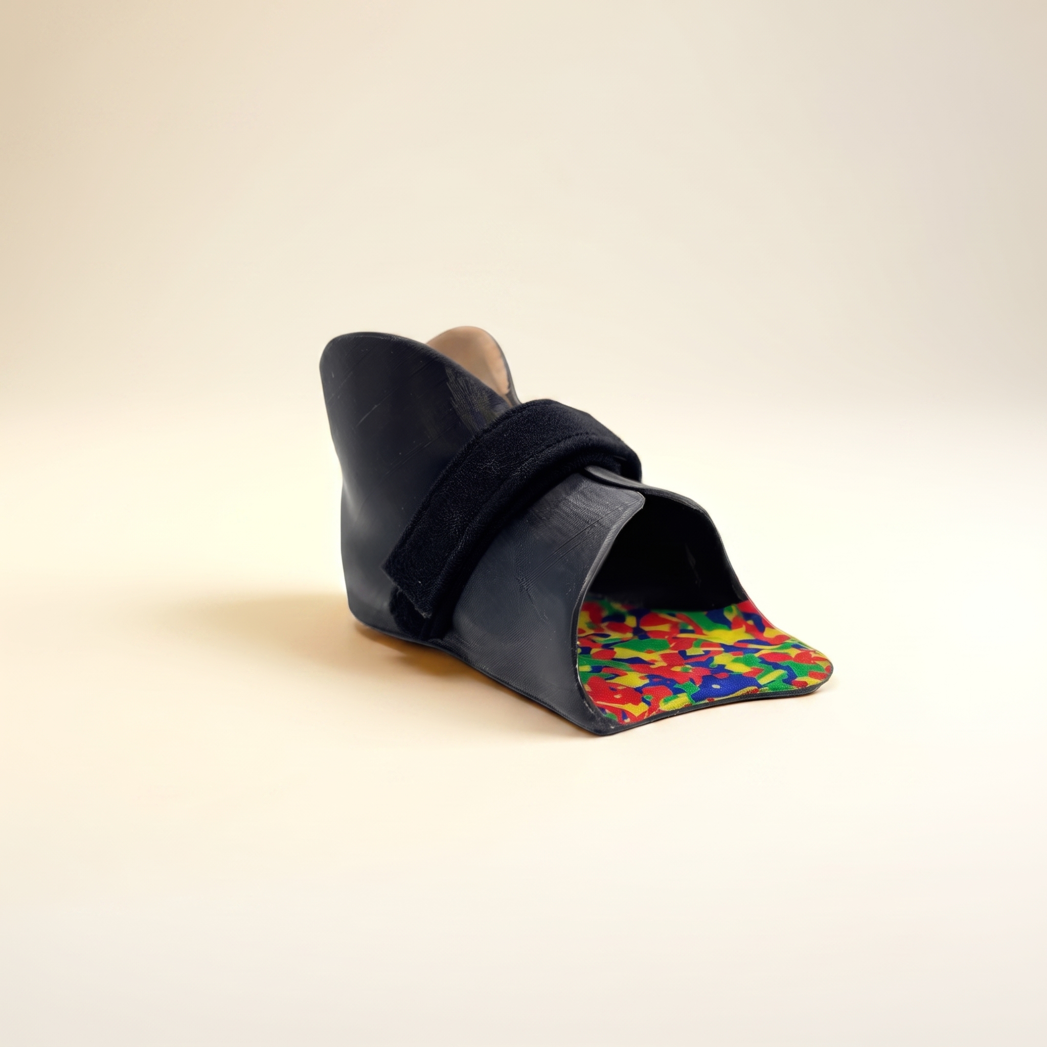 Black orthopedic shoe with colorful insole and strap on a plain beige background.