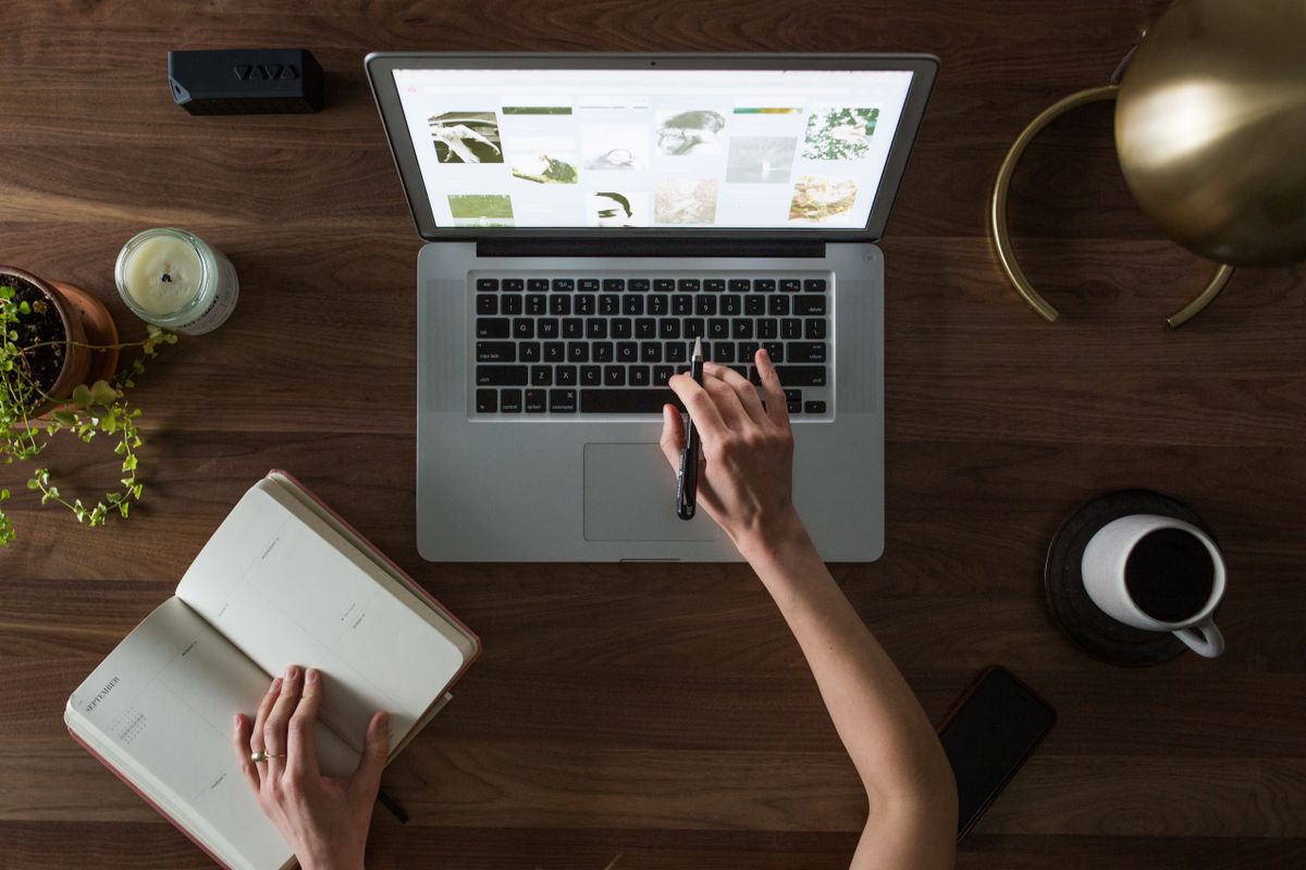 A laptop, planner notebook, pen, and coffee on a desk, set up for planning