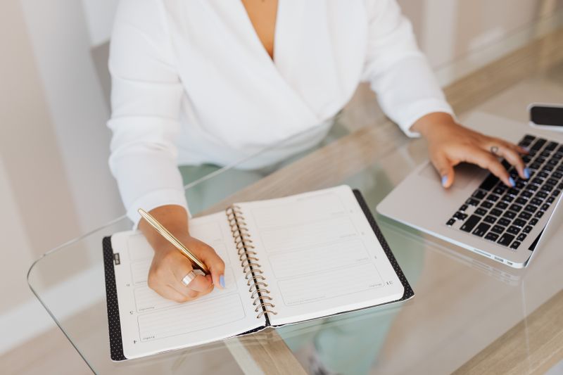 A person writing goals in a notebook beside a laptop, representing AI-assisted life planning