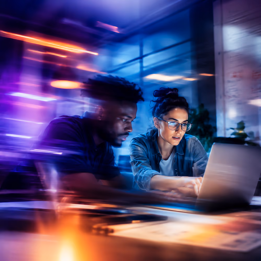 Two people working intensely together at a laptop in a modern office with colorful motion blur lights.