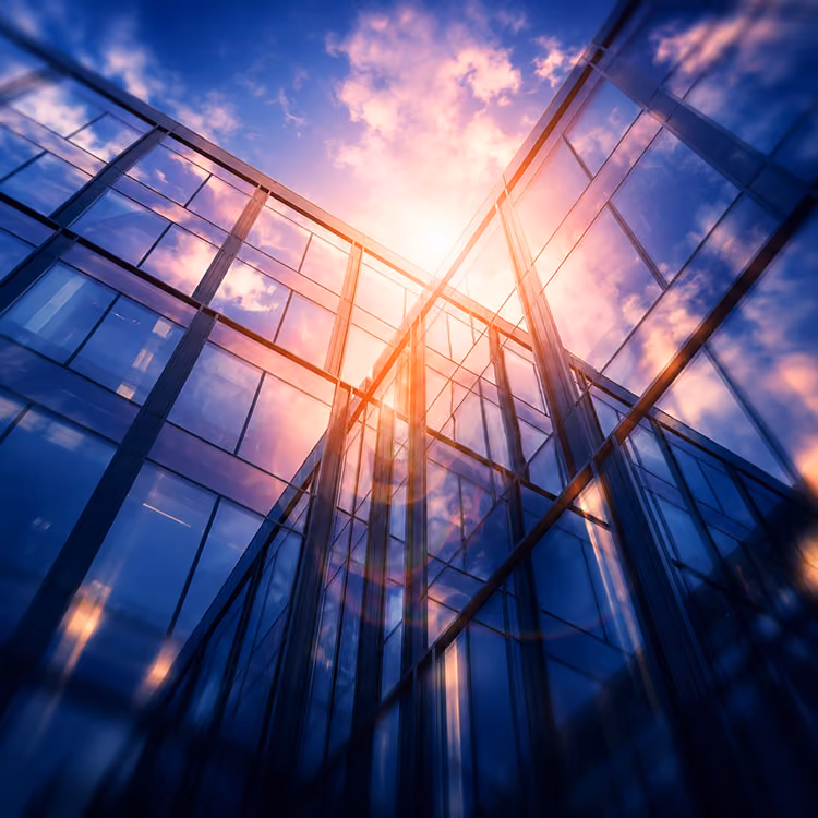 Sunlight shines through the glass facade of a modern high-rise building with sky reflections.