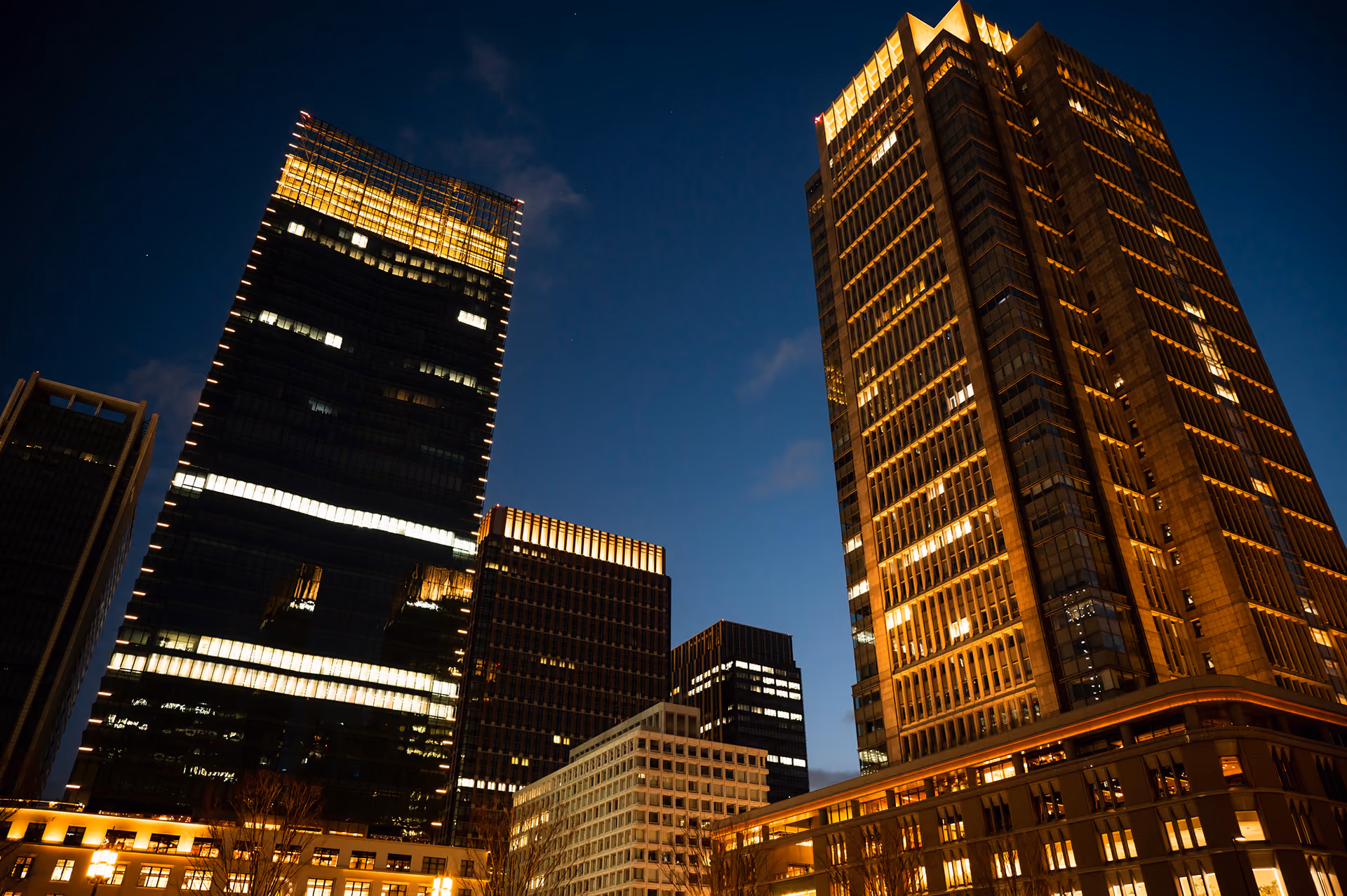 Illuminated modern skyscrapers at night against a dark blue sky in a cityscape.