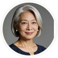 Portrait of a smiling older woman with short gray hair and pearl earrings against a gray background.