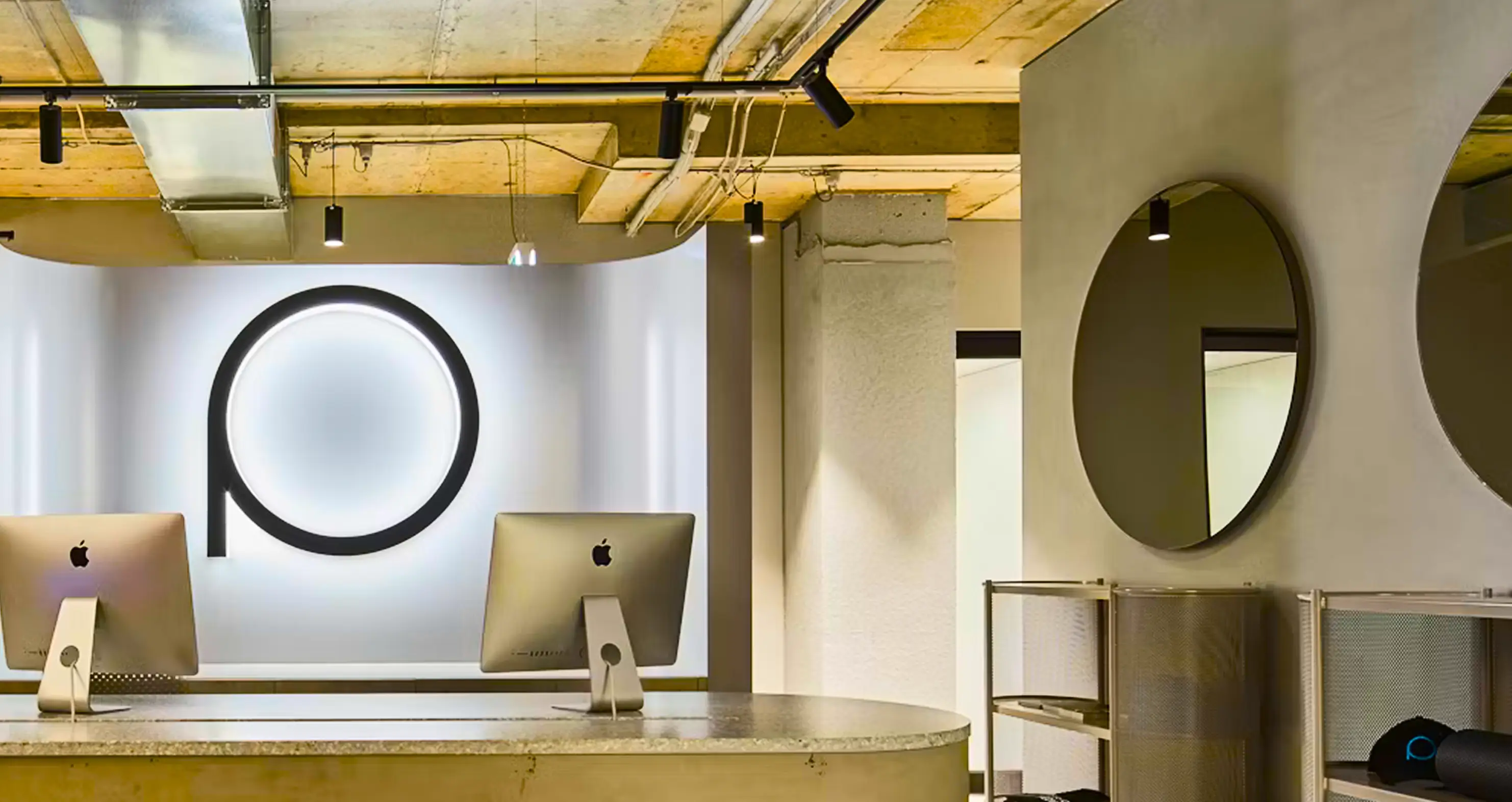 Modern reception desk with two Apple computers and a circular lighted logo on the back wall.