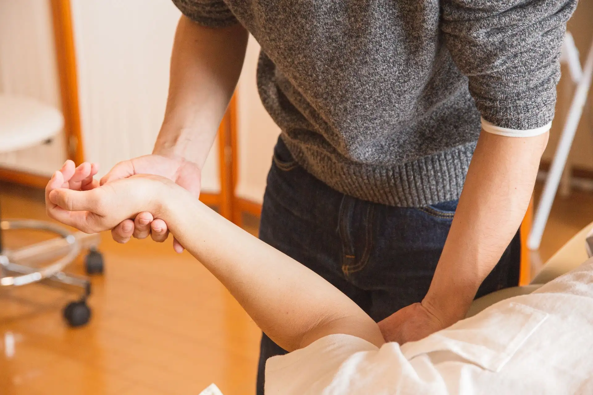Therapist or doctor examining patient's forearm in a clinical or therapy setting.