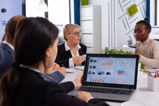 Four business professionals in a meeting room focusing on a laptop screen displaying charts and graphs.