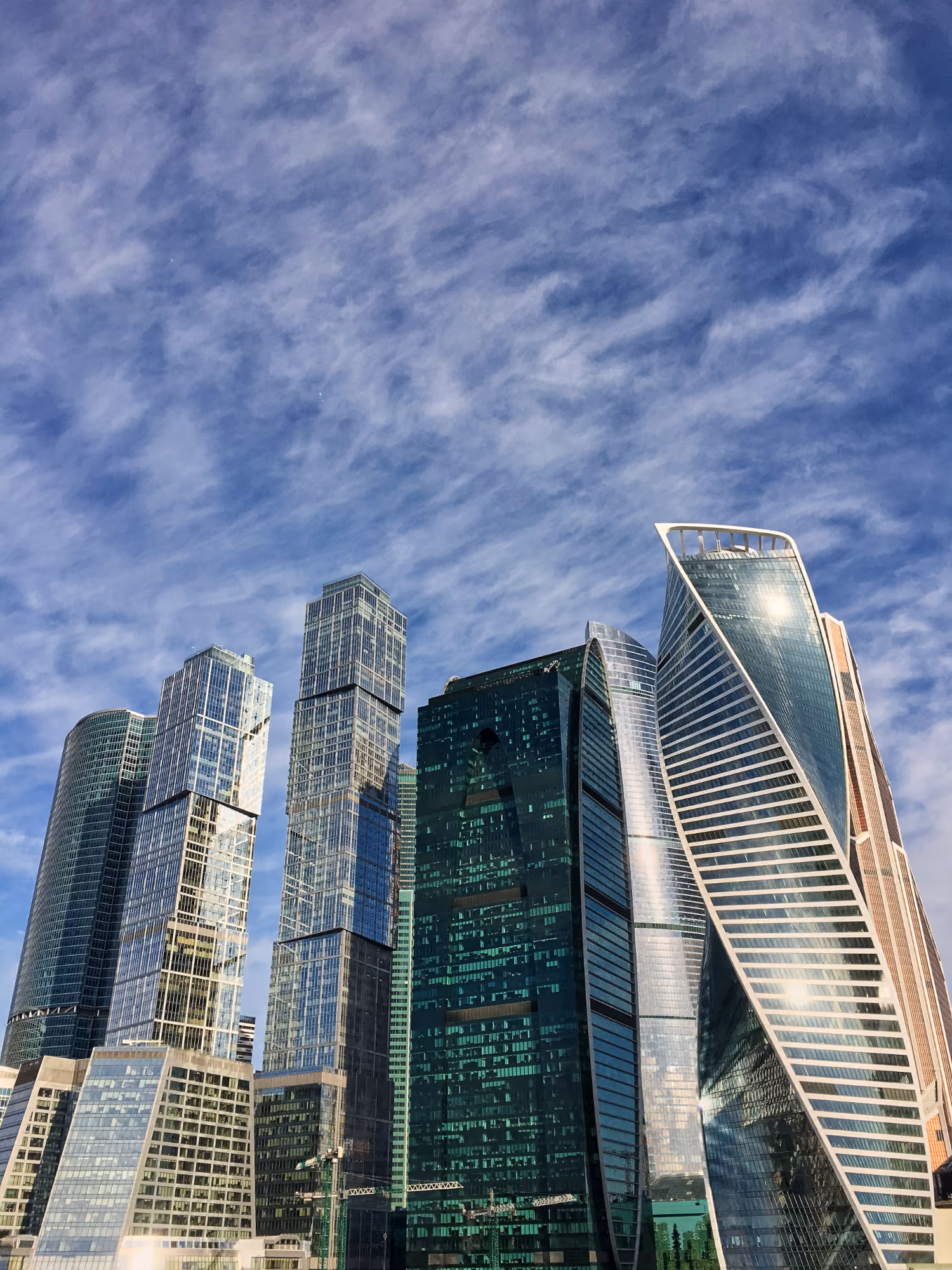 Cluster of modern skyscrapers with glass facades under a blue sky with scattered clouds.