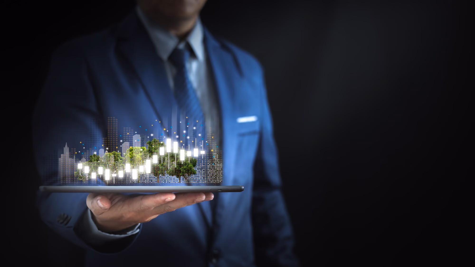 Businessman in a blue suit holding a tablet projecting a digital 3D cityscape with green trees and illuminated buildings and data graphs.