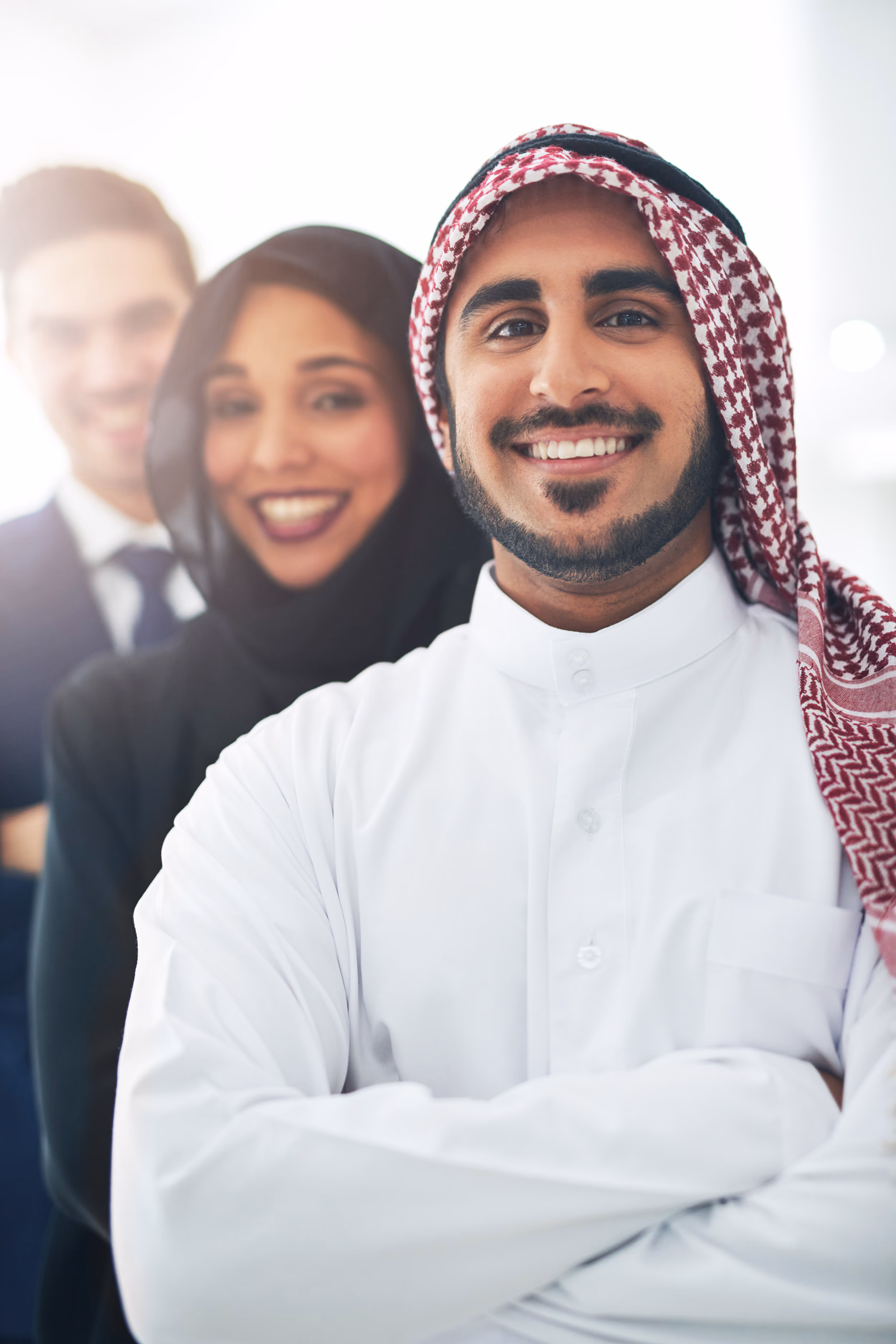 Smiling Middle Eastern businessman in traditional white attire standing with two business colleagues in an office.