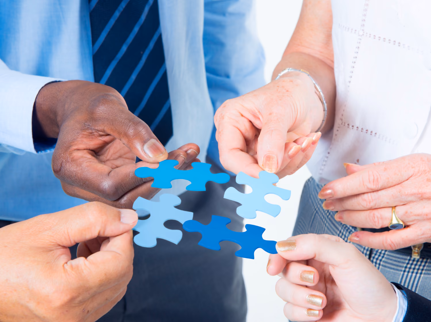 Four people holding interconnected blue puzzle pieces, symbolizing teamwork and collaboration.