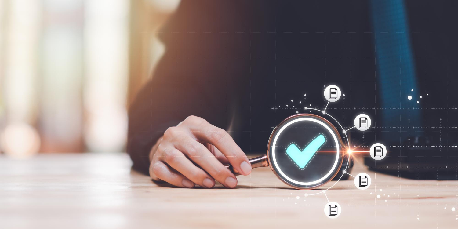 A hand holding a magnifying glass over a wooden surface with a glowing blue checkmark visible inside and various document icons connected around it, symbolizing verification or approval.