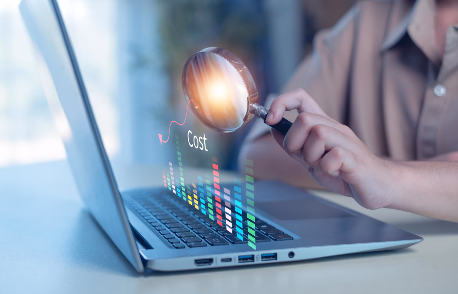 Person holding a magnifying glass over a laptop keyboard highlighting the word 'Cost' and colorful digital bar graph data.