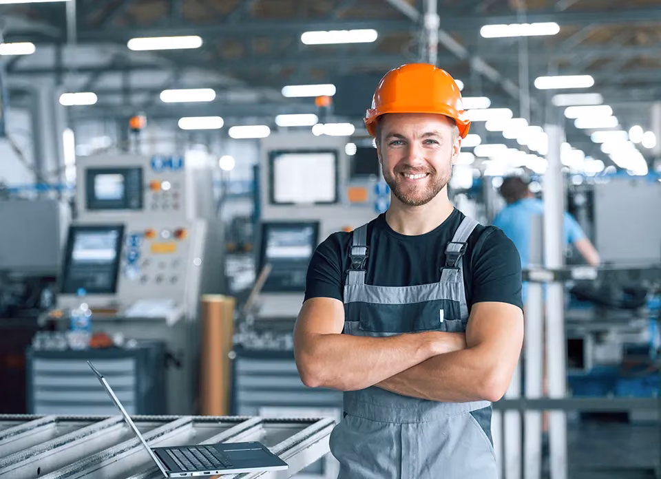 Technicien souriant en casque orange, bras croisés, dans un atelier de production