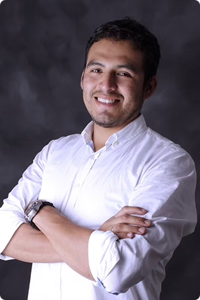 Smiling man with short dark hair and a beard in a white buttoned shirt against a dark background.