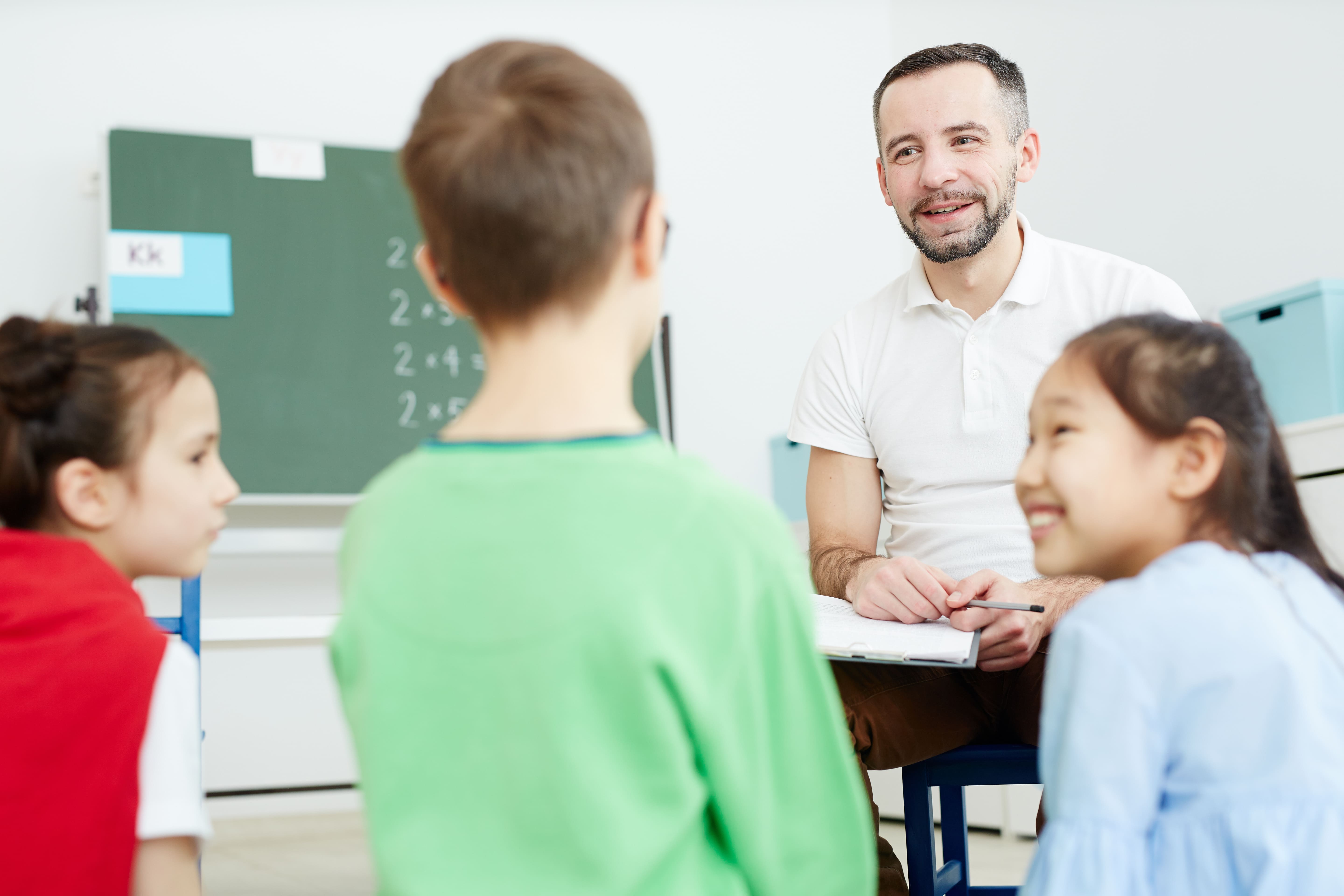 Care service apprebtice smiling and sitting on a chair facing three young children in a classroom