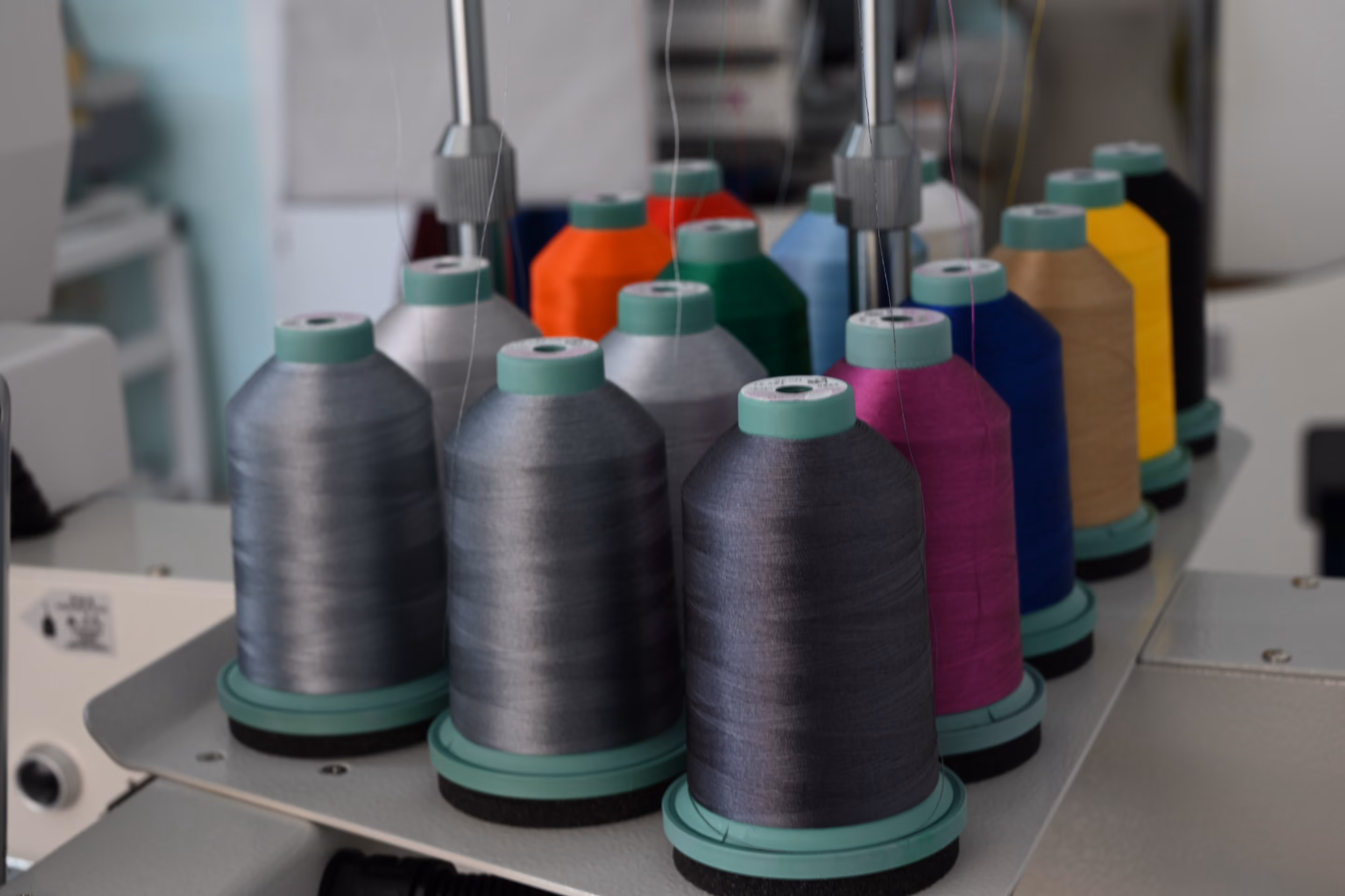 Verschiedene bunte Garnspulen auf einer Garnhalterung einer industriellen Nähmaschine.