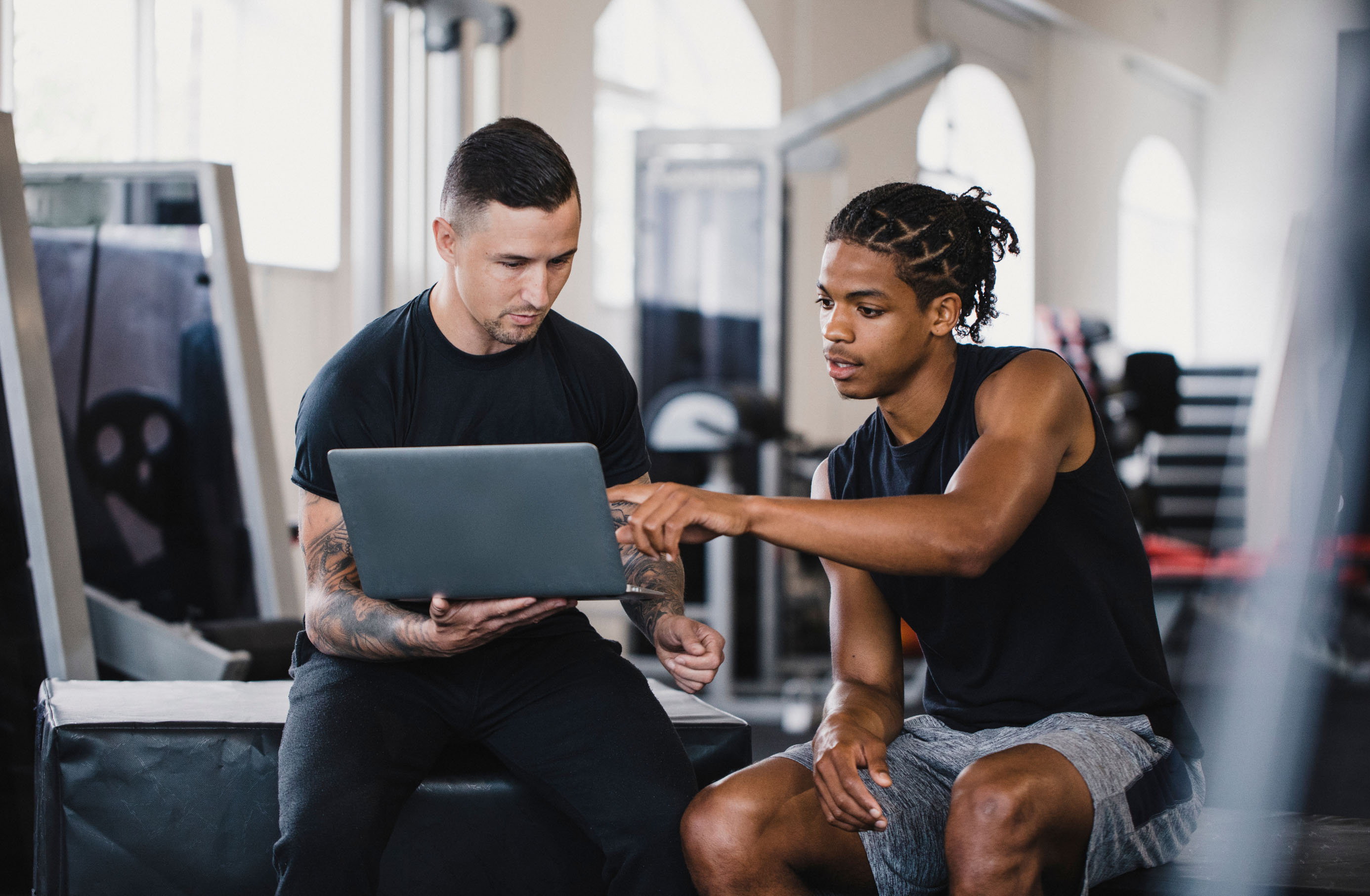 a man showing a laptop to a man in a gym