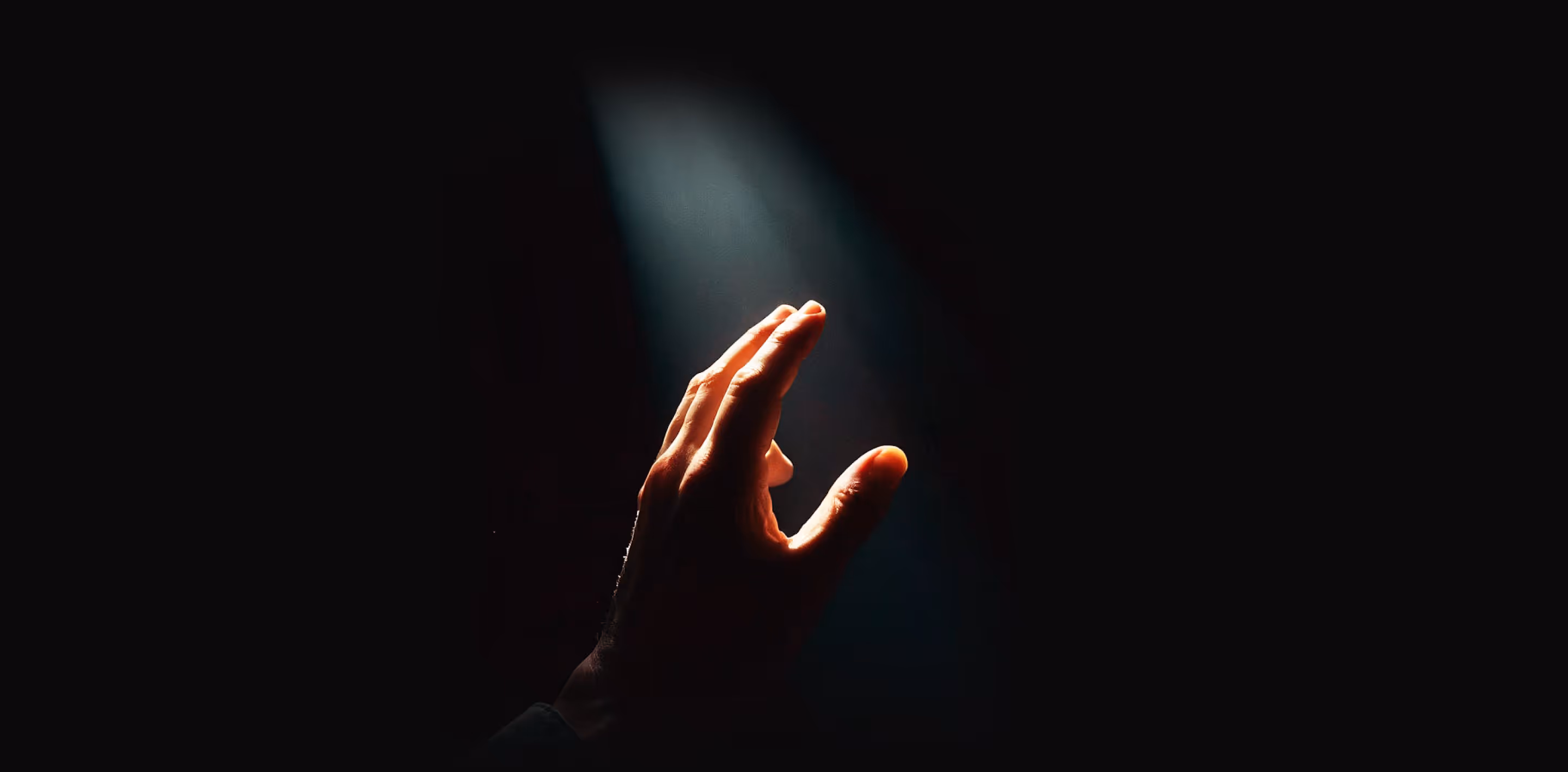 Hand partially illuminated reaching towards a beam of light in a dark background.
