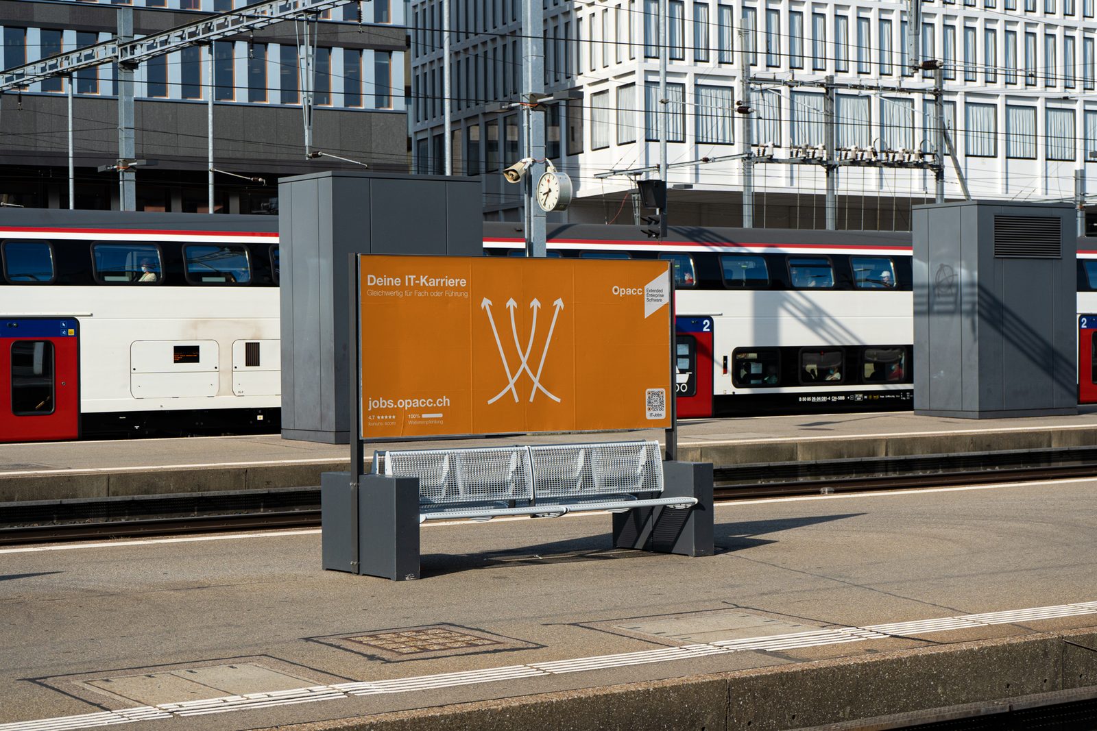F12-Plakat der Opacc Kampagne Deine IT-Karriere an einem Bahnperron, Pfeilmotiv auf Orange.