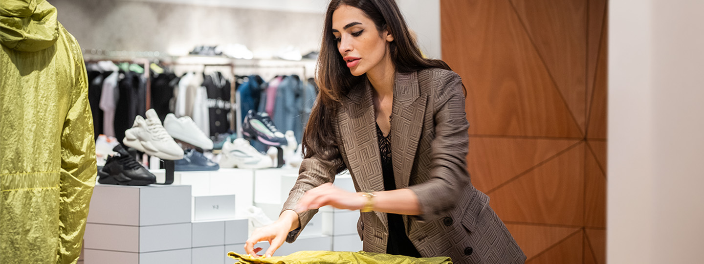 Globus Verkaufsberaterin in kariertem Blazer faltet ein Kleidungsstück in der Modeabteilung.