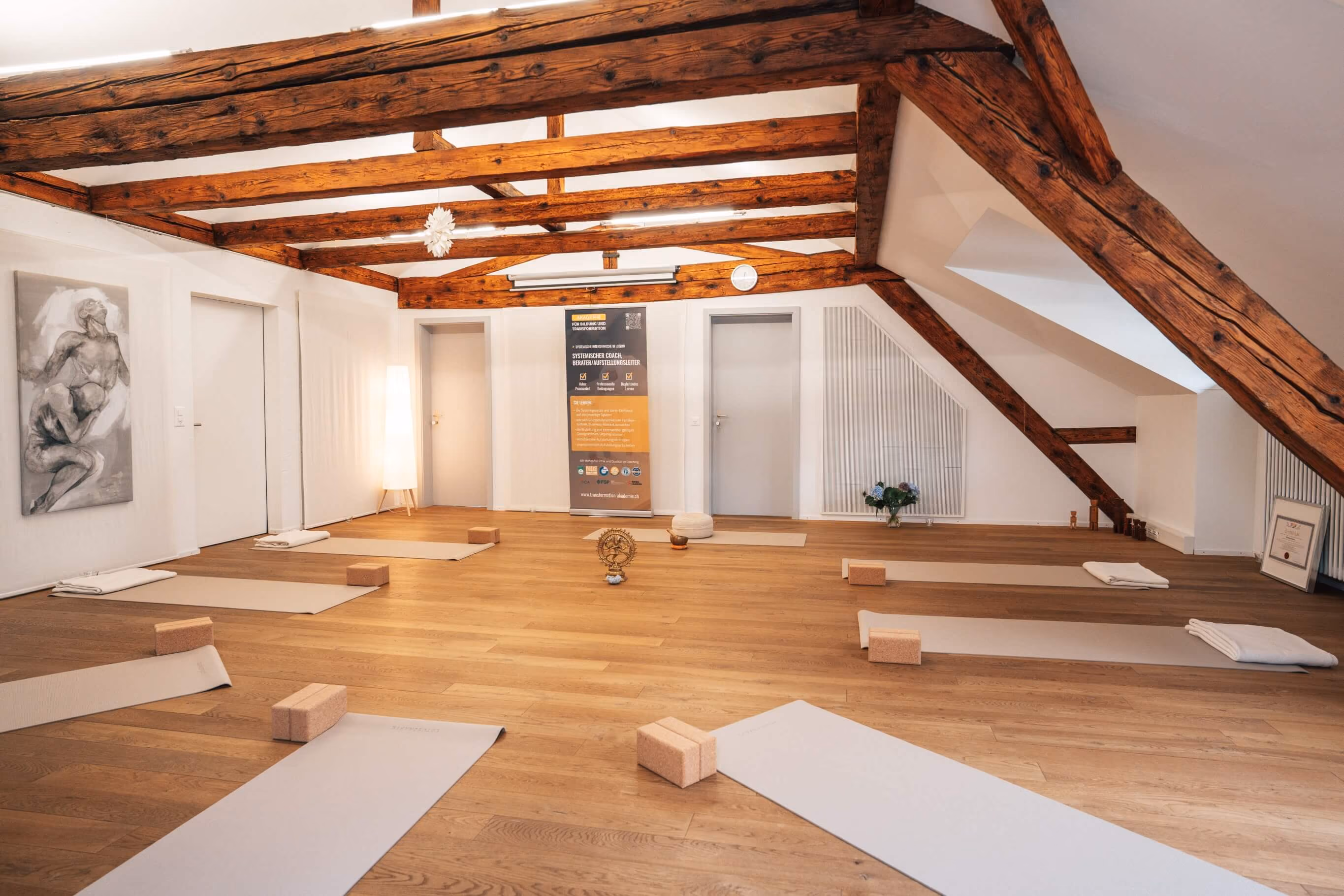 Heller Yoga- und Meditationsraum in der Akademie für Bildung und Transformation in Luzern mit Yogamatten, Korkblöcken, Decken und Sitzkissen.