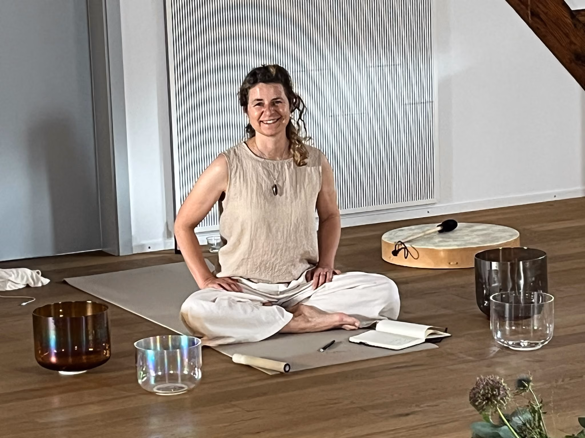 Yvonne Zürcher sitzt auf einer Matte im hellen Raum, umgeben von Klangschalen und Trommeln für Breathwork und Klangarbeit in der Akademie für Bildung und Transformation in Luzern.