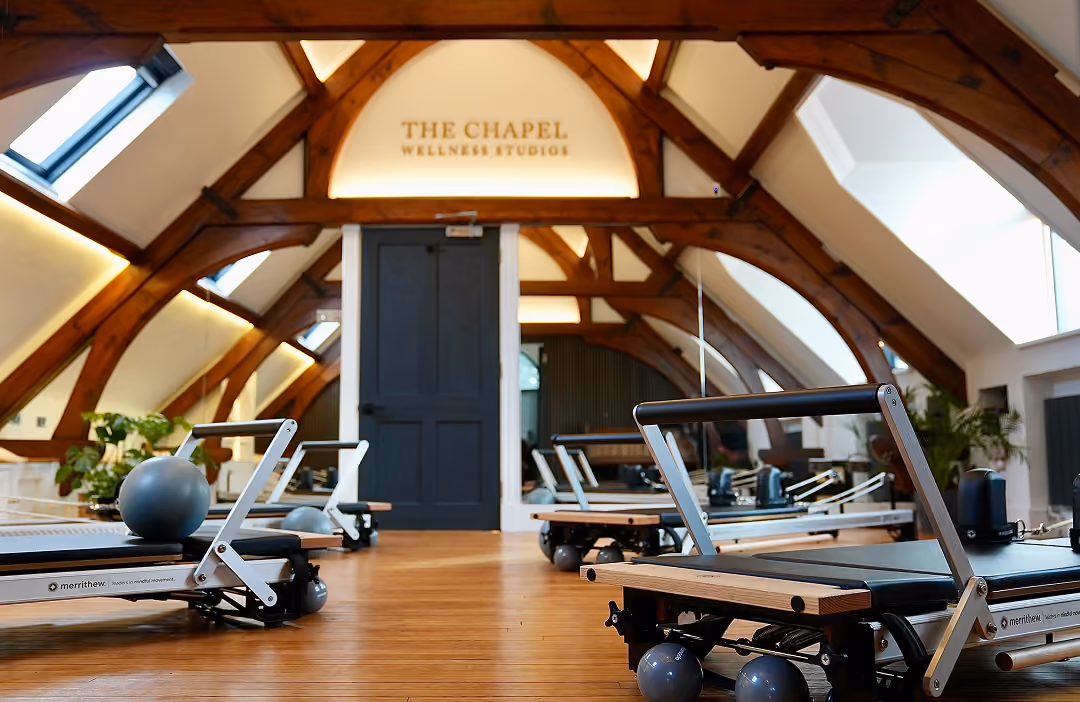Interior of The Chapel Wellness Studios with wooden beams, skylights, and exercise reformer machines on a wooden floor.