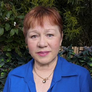 Portrait of Wilhelmina Ligthart, founder and managing director of Intertradedocs, standing outdoors in front of green leafy plants.