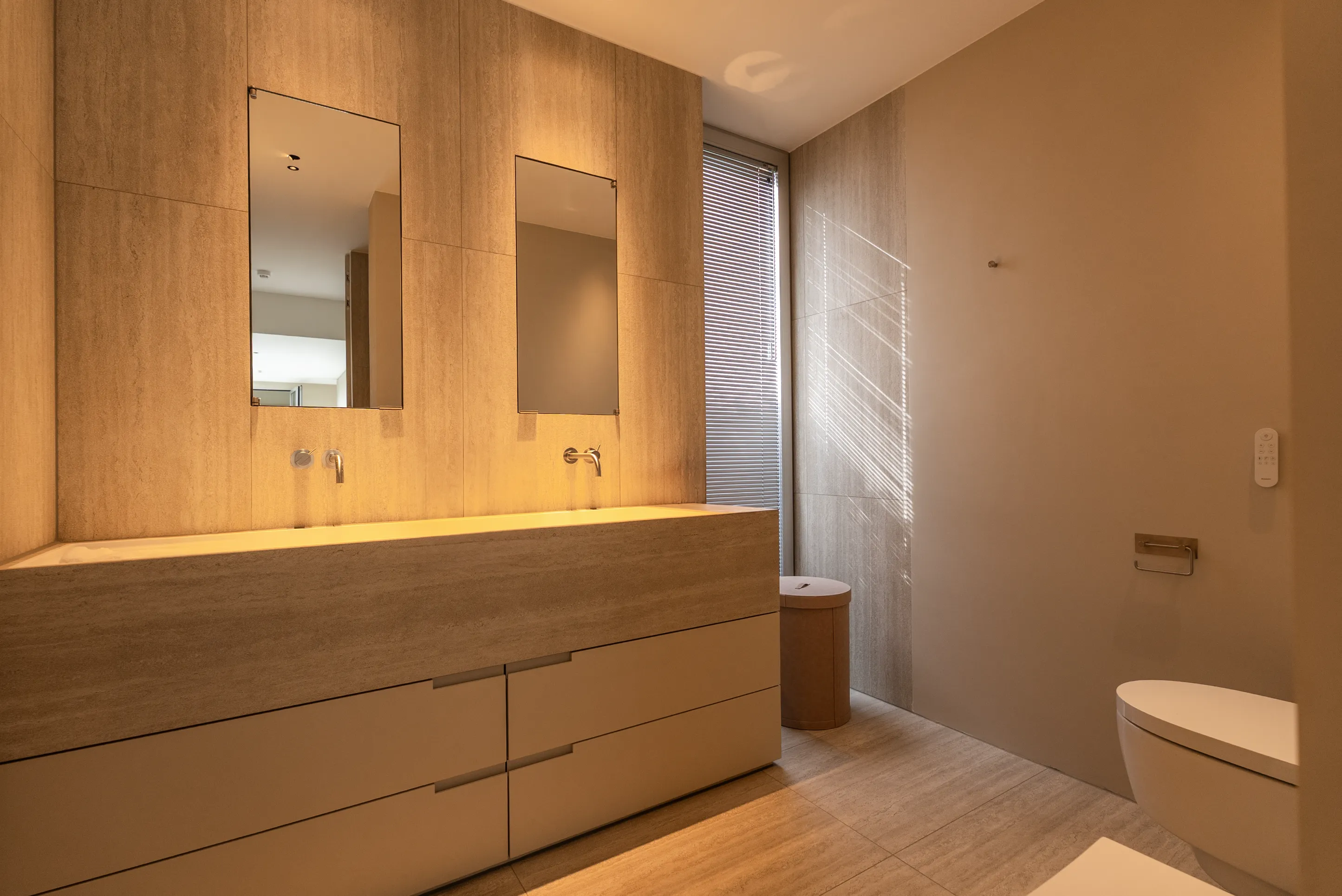 Badkamer met zwevend wastafelmeubel, twee spiegels en natuurstenen wandbekleding