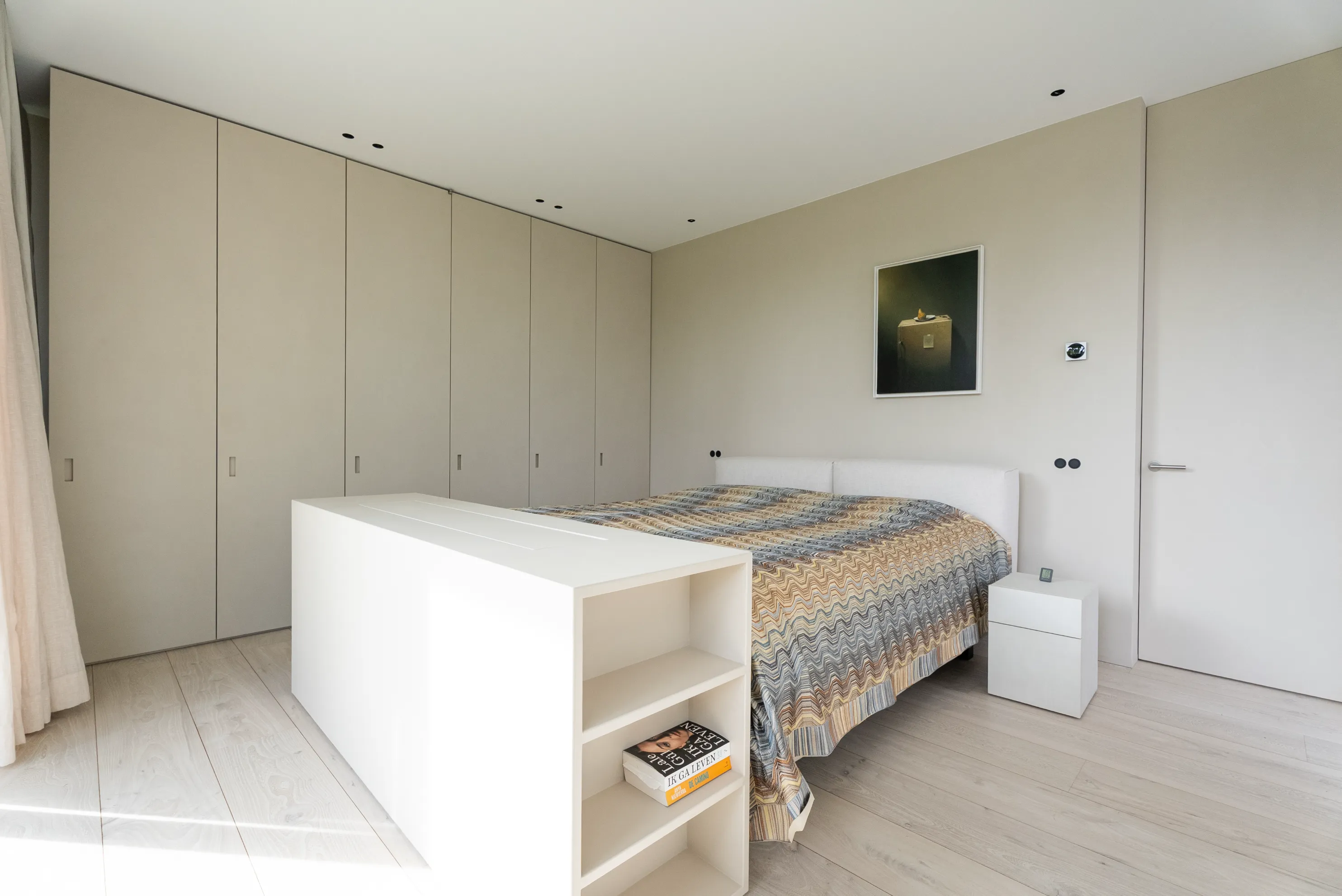 Slaapkamer met inbouwkasten over de volle wandbreedte en een lichte houten vloer