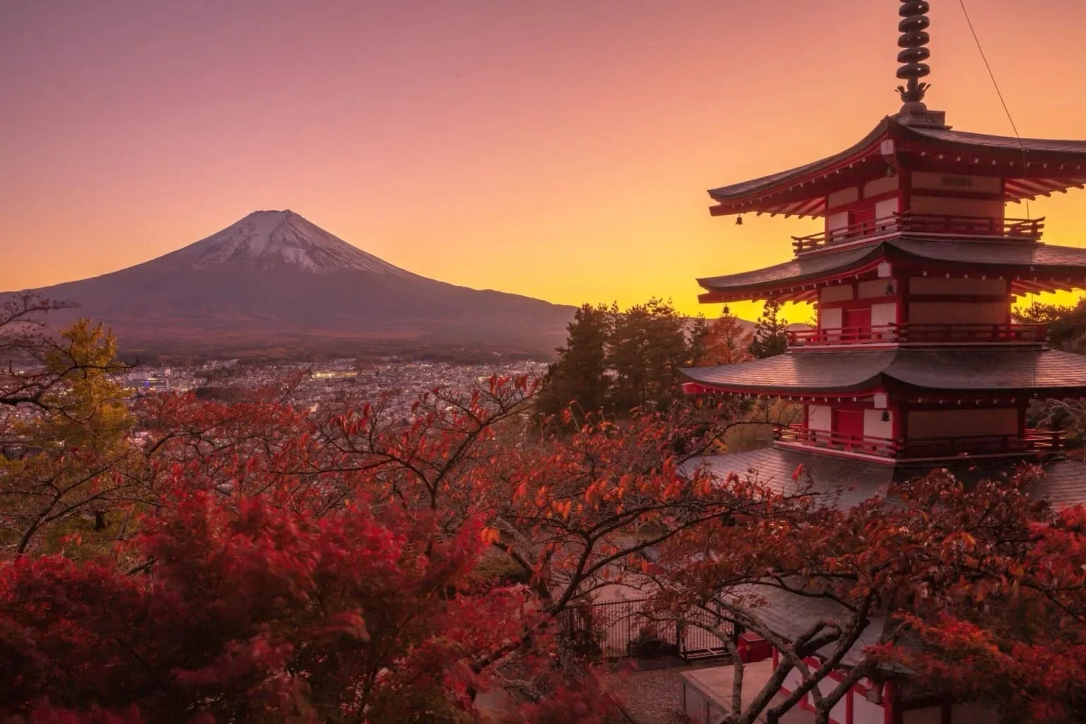 Mount Fuji at sunset with a red pagoda framed by autumn maple leaves