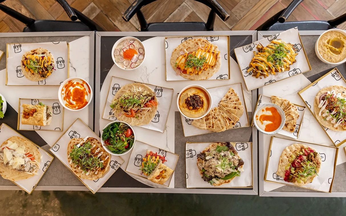 Le Bab kebabs, hummus and salads in branded paper trays on a long table