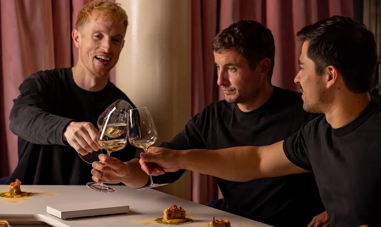 Three friends raising wine glasses over a table of small plates