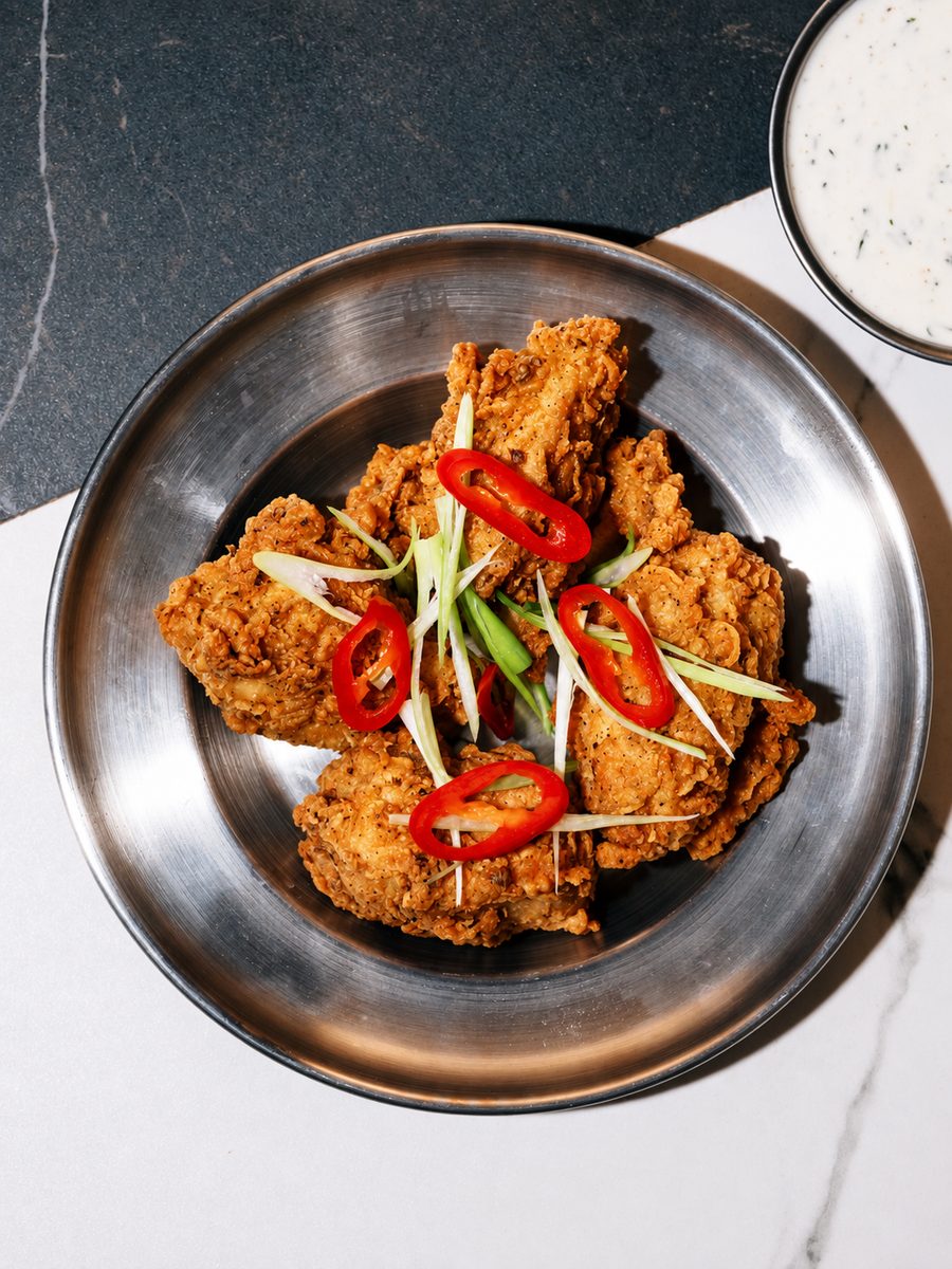 Fried chicken with sliced red chilli and spring onion in a steel bowl