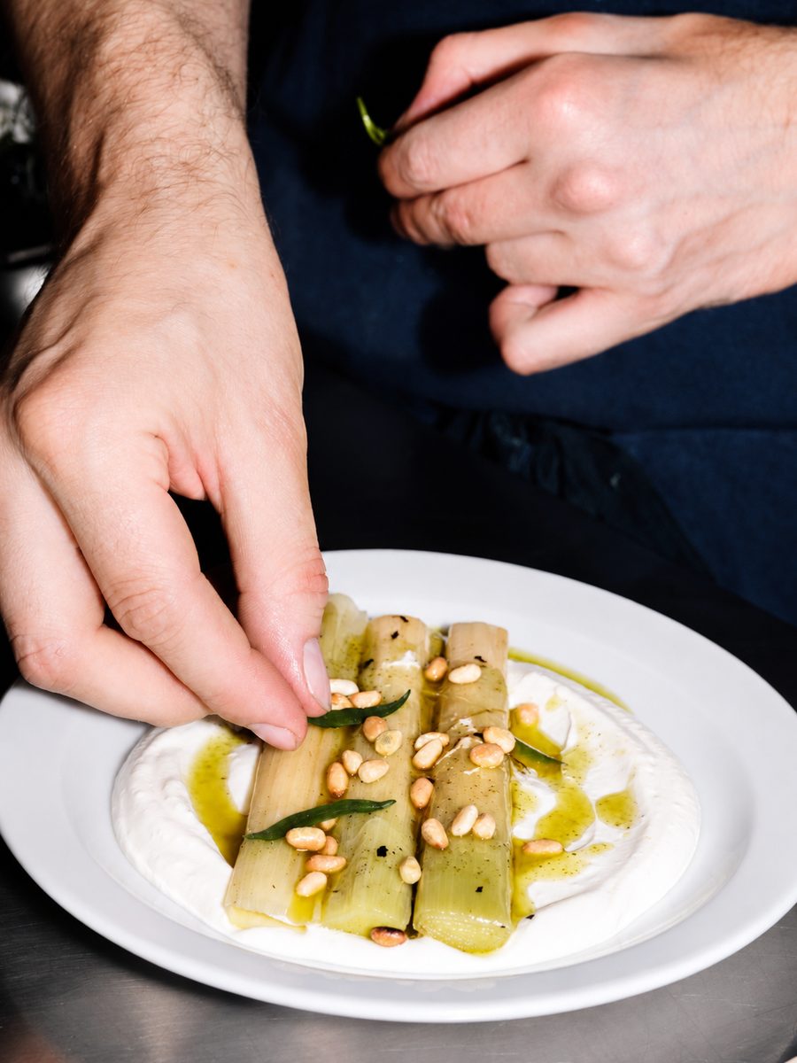 A chef plating charred leeks on whipped labneh with pine nuts