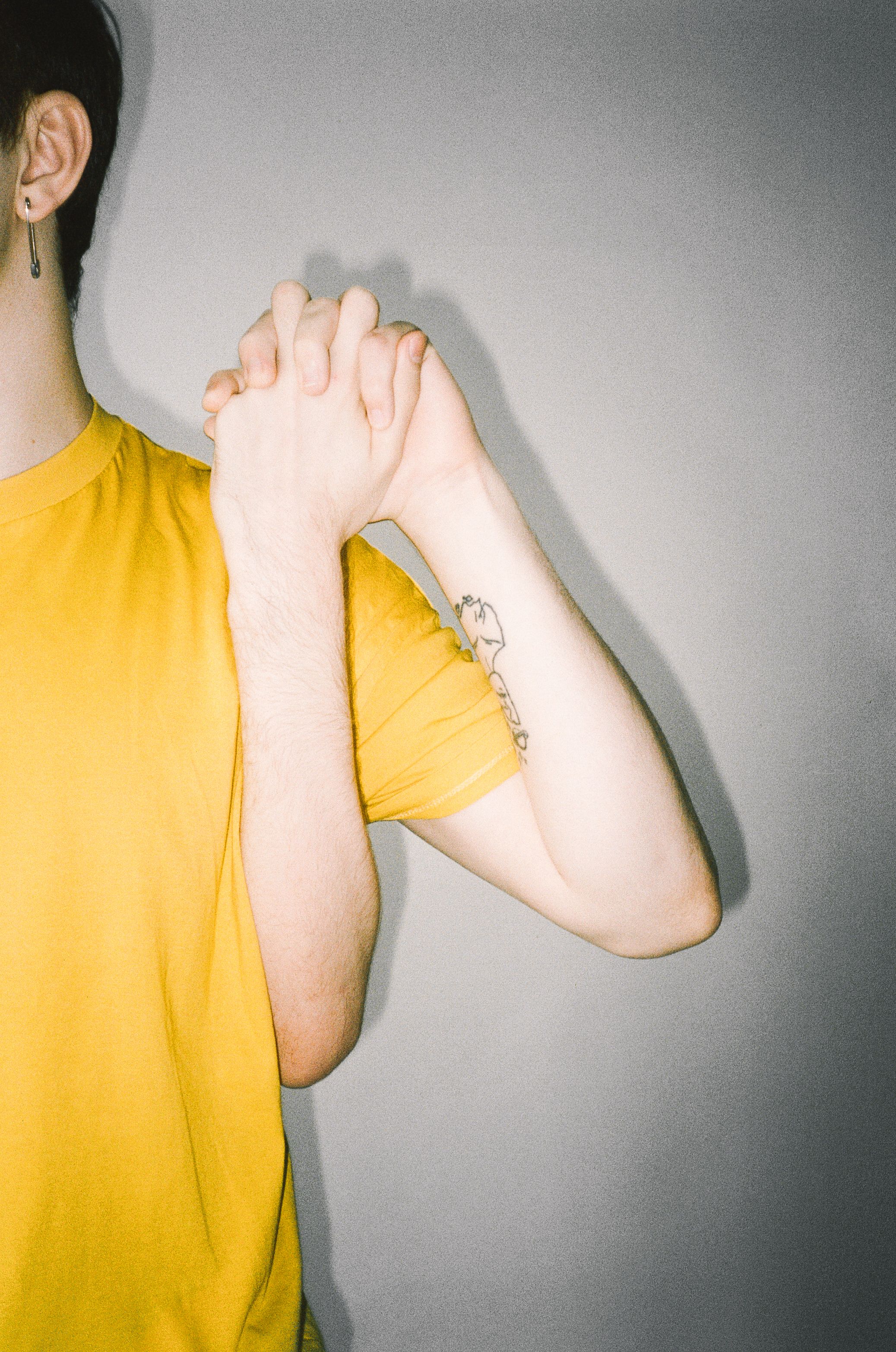 Person in yellow shirt holding hands clasped tightly against a gray background.