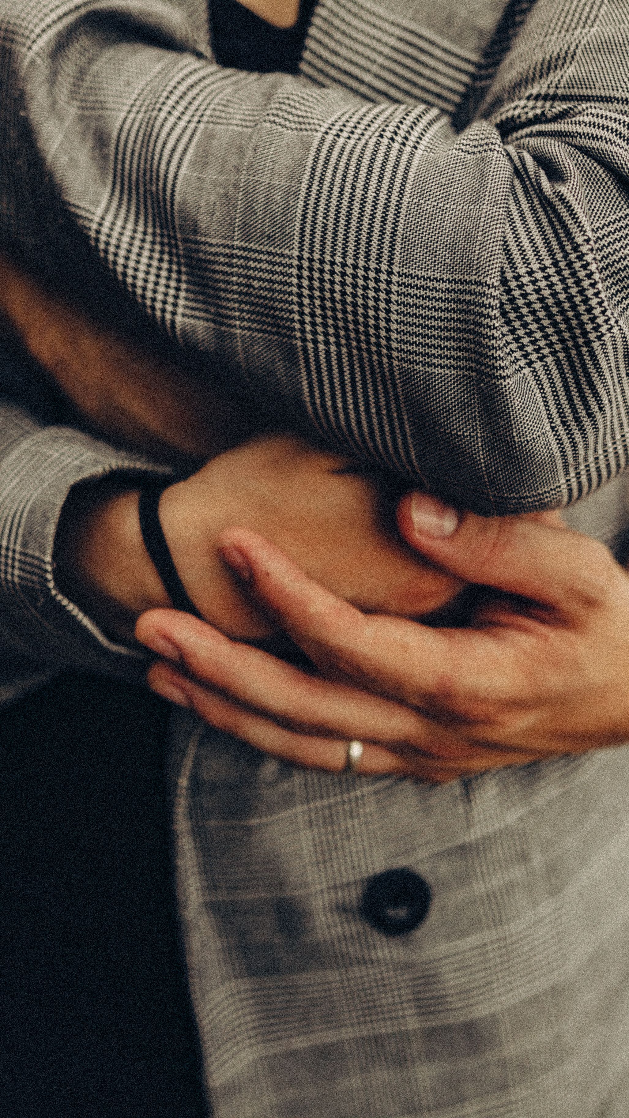 Hands gently holding an arm wearing a gray plaid coat with a button.