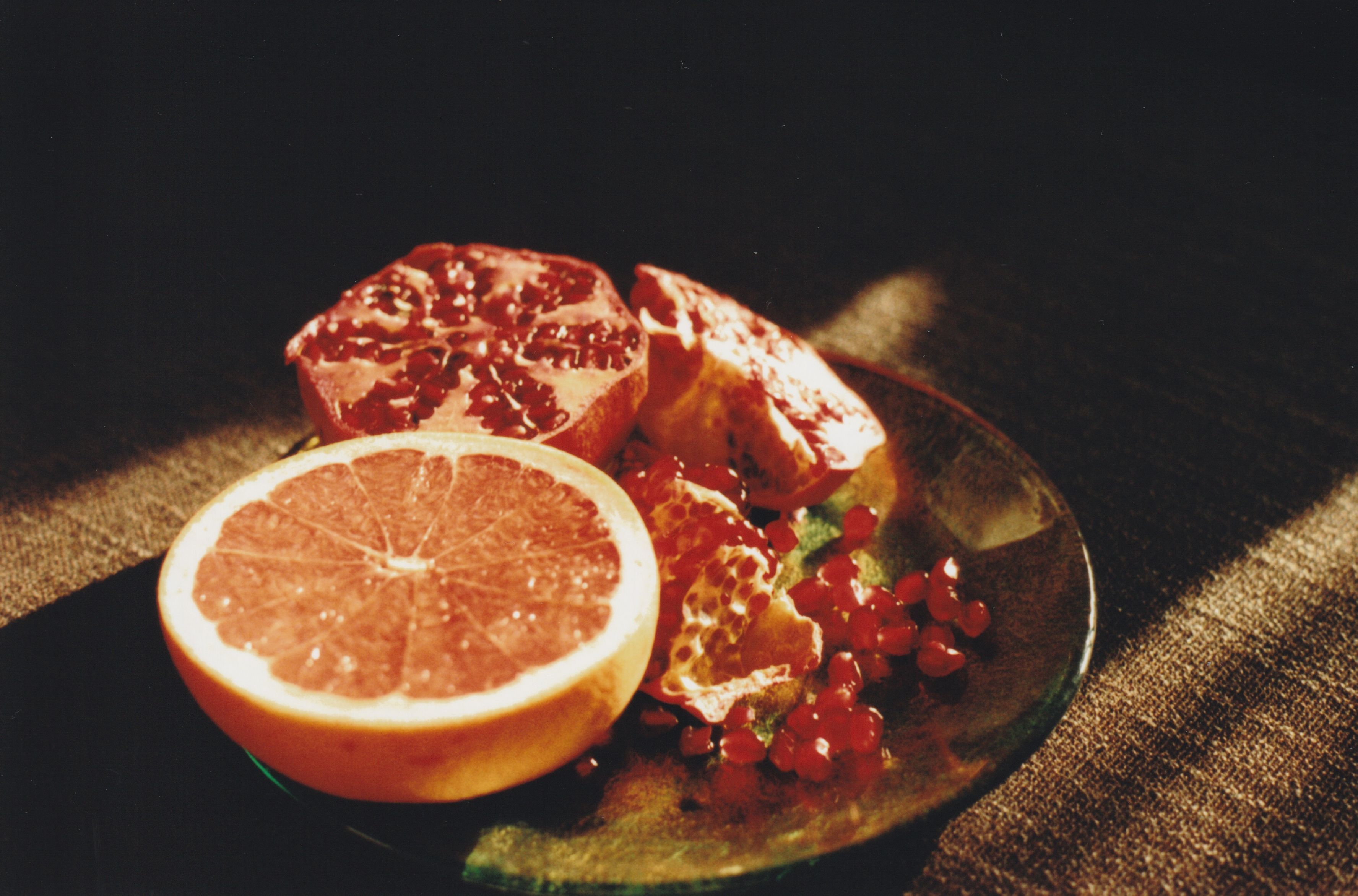 Half a grapefruit and pomegranate seeds on a glass plate with warm sunlight and shadows.