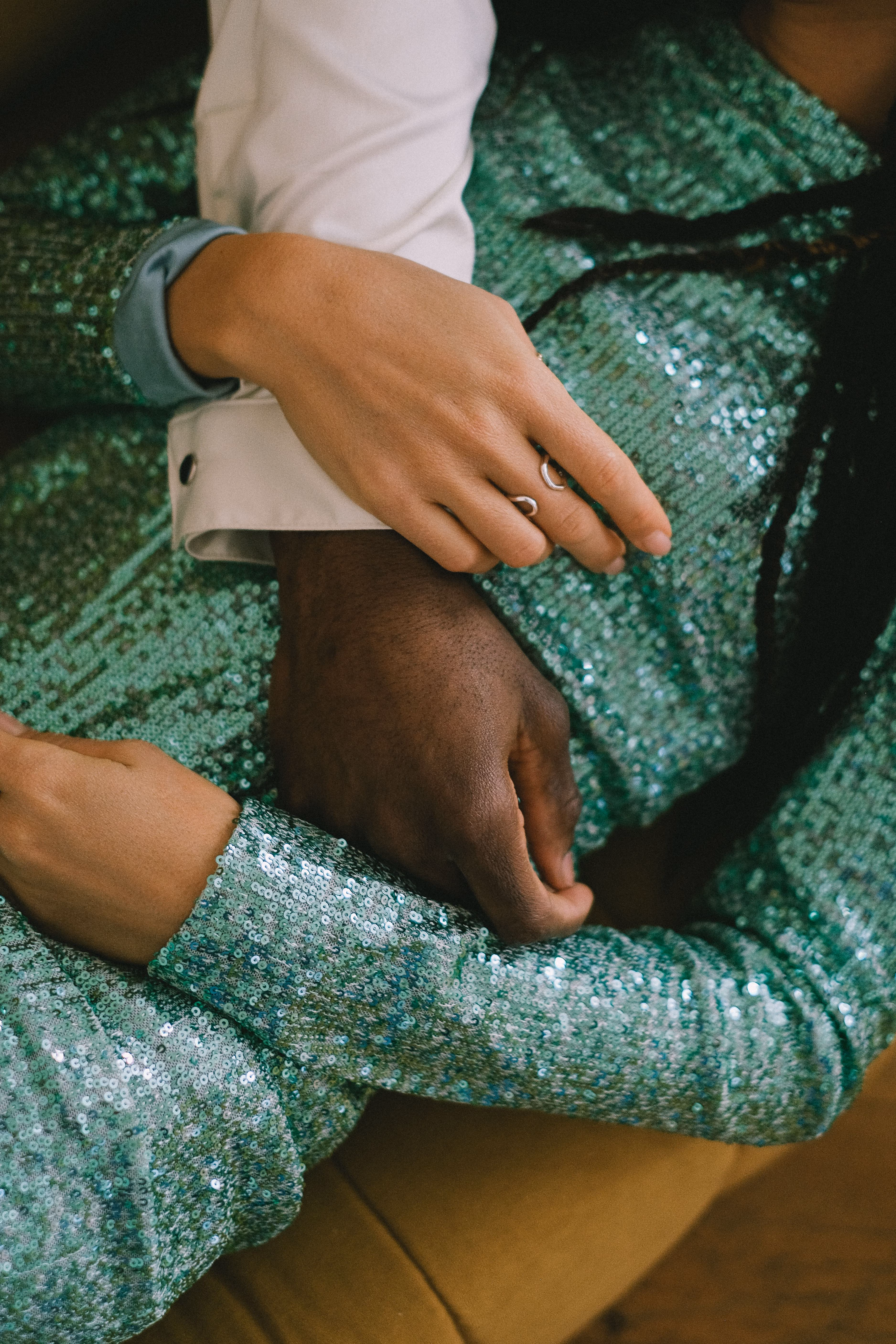Close-up of two people embracing, wearing sparkling green sequin outfits and rings on hand.