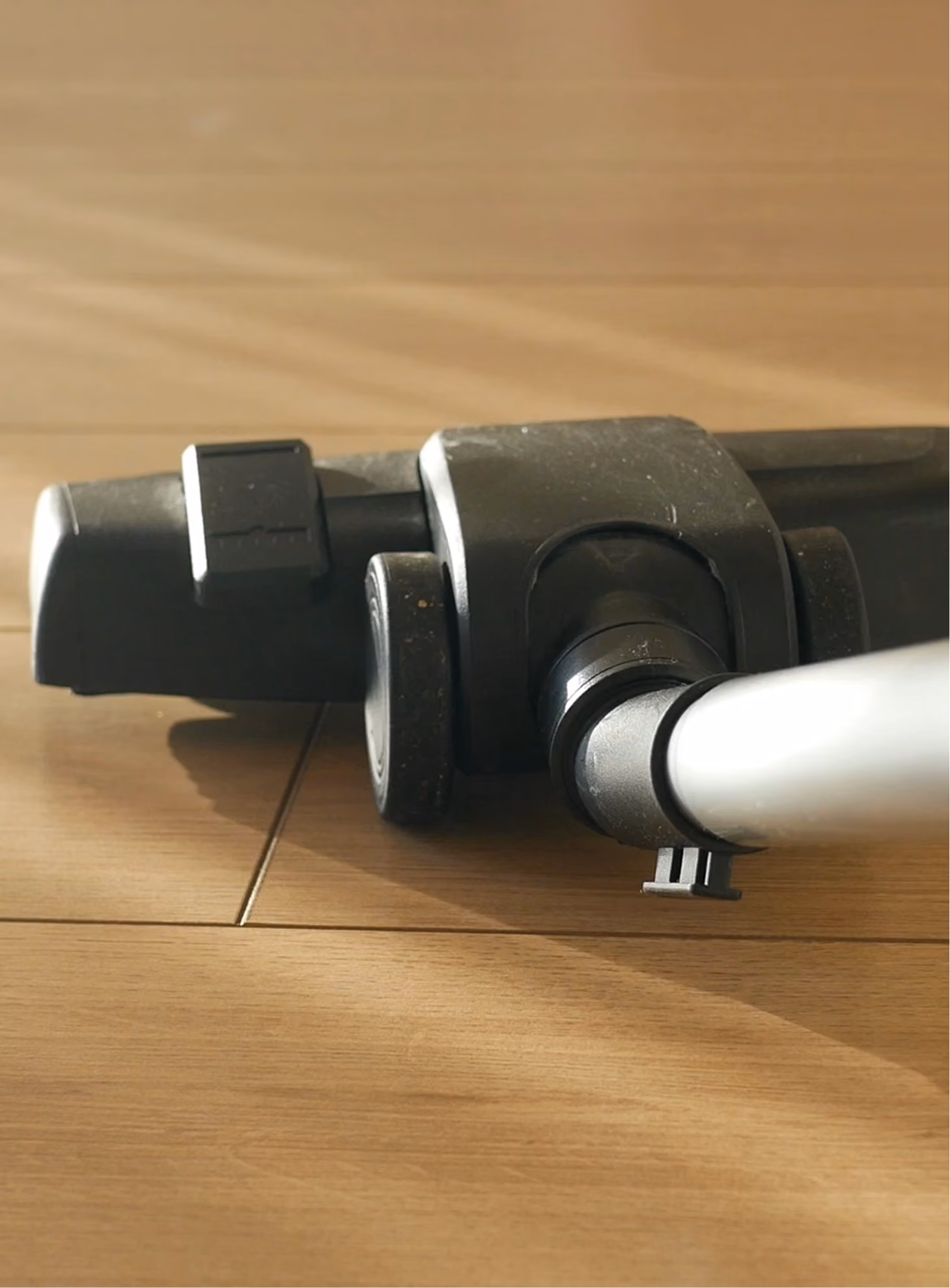 Close-up of vacuum cleaner head with wheels on a wooden floor.