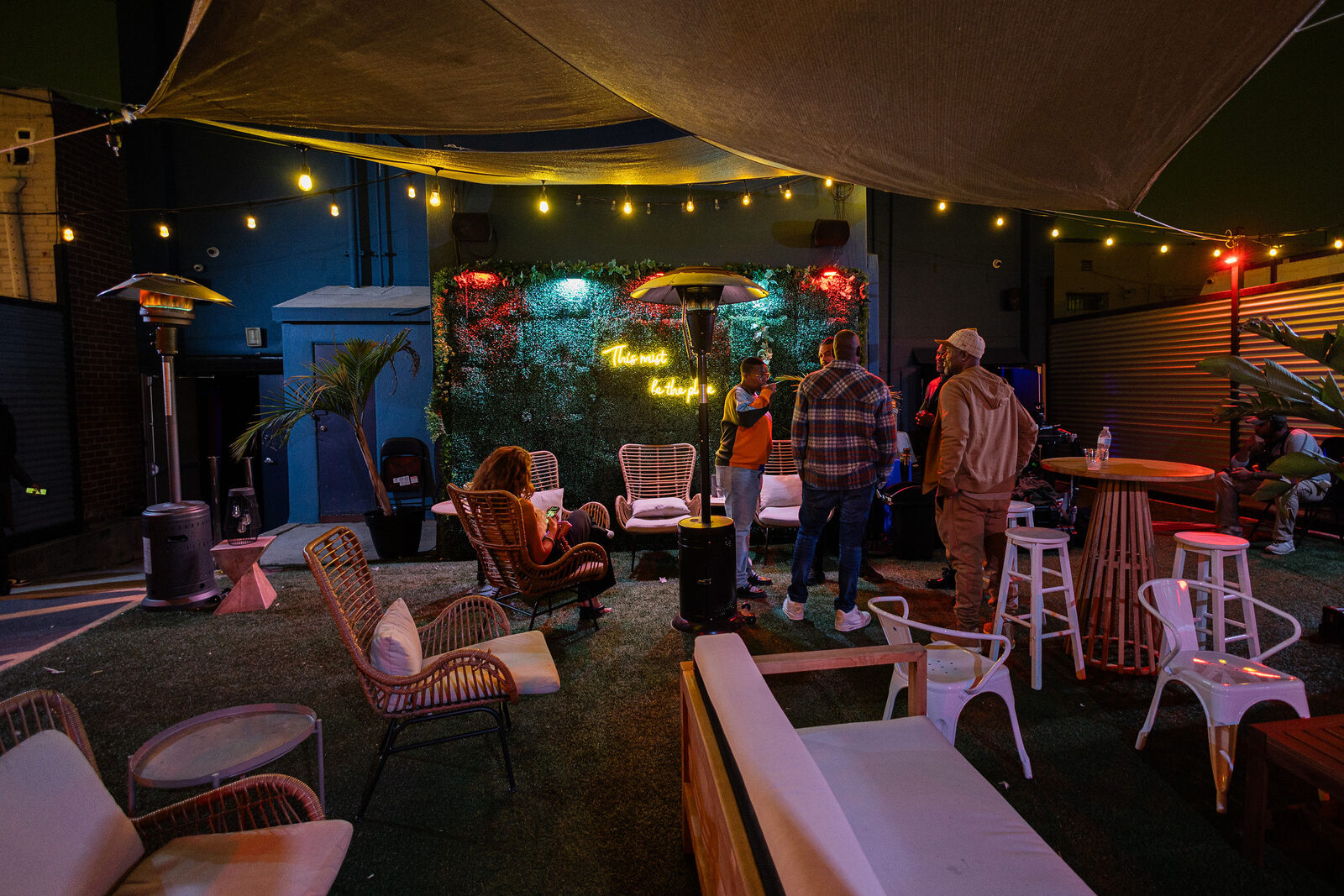The backyard at night: string lights, heat lamps, rattan lounge seating and the neon sign on the greenery wall