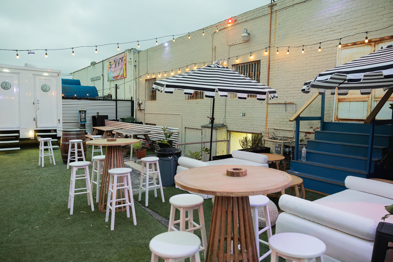 Striped umbrellas, high tables and daybeds set up across the backyard turf
