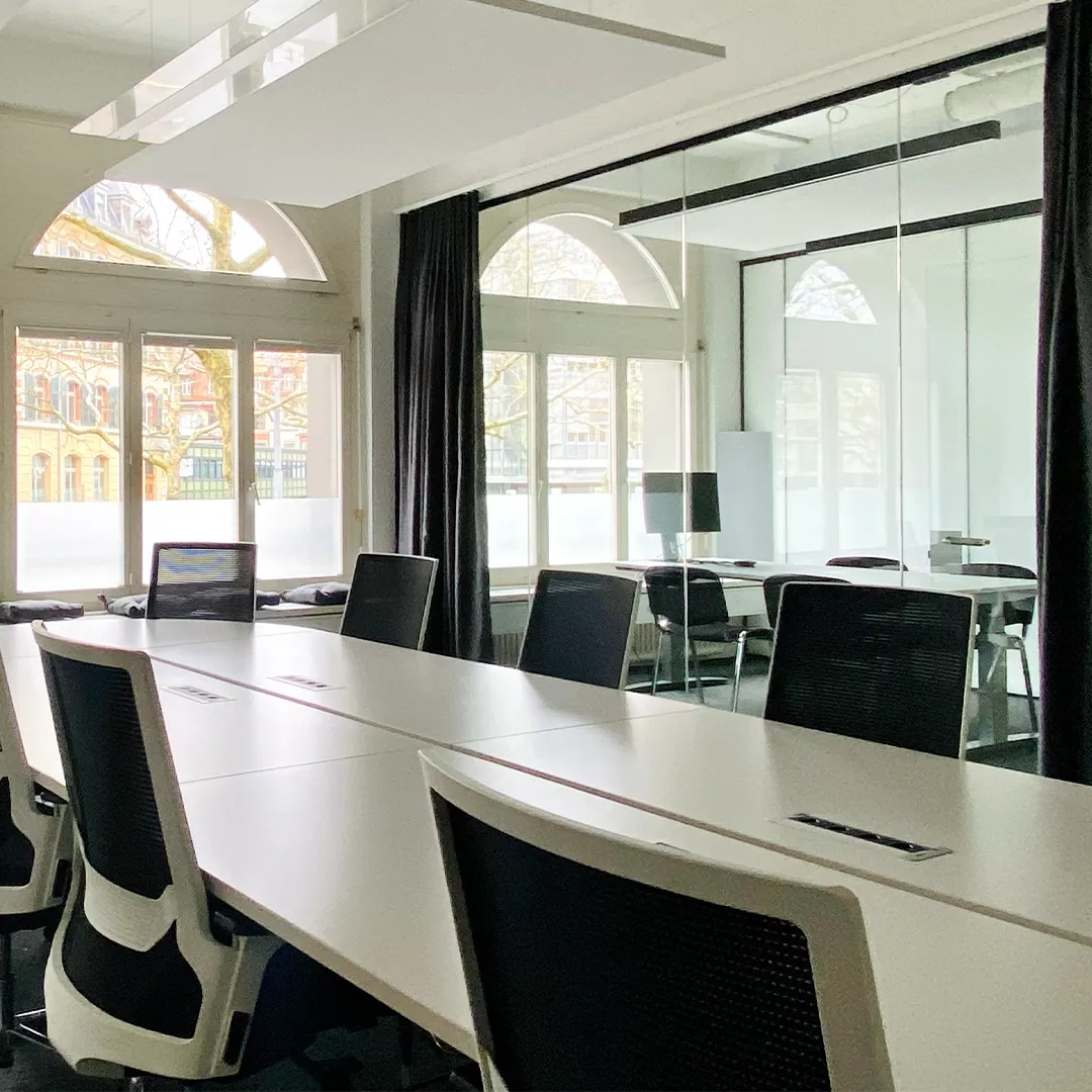 Modernes Bürodesign mit hellem Sitzungszimmer, langen Besprechungstischen und verglaster Raumtrennung