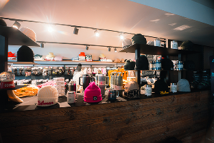 Comptoir en bois avec plusieurs bonnets exposés en première ligne dans une boutique éclairée, avec des étagères en arrière-plan contenant divers articles.